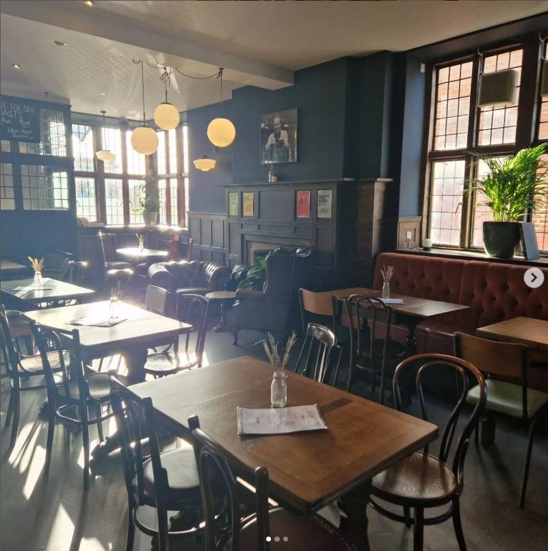 Spacious pub dining room location house in Lewisham SE6 through Love Locations, featuring dark wood dining sets, ambient pendant lighting, and dark green walls.