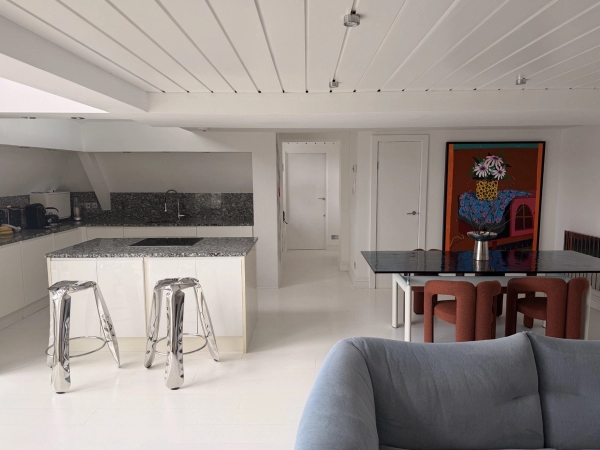 Modern white kitchen and dining space in a Brixton SW4 converted school loft available via Love Locations, showcasing a white kitchen island, chrome bar stools, and crisp white ceilings.