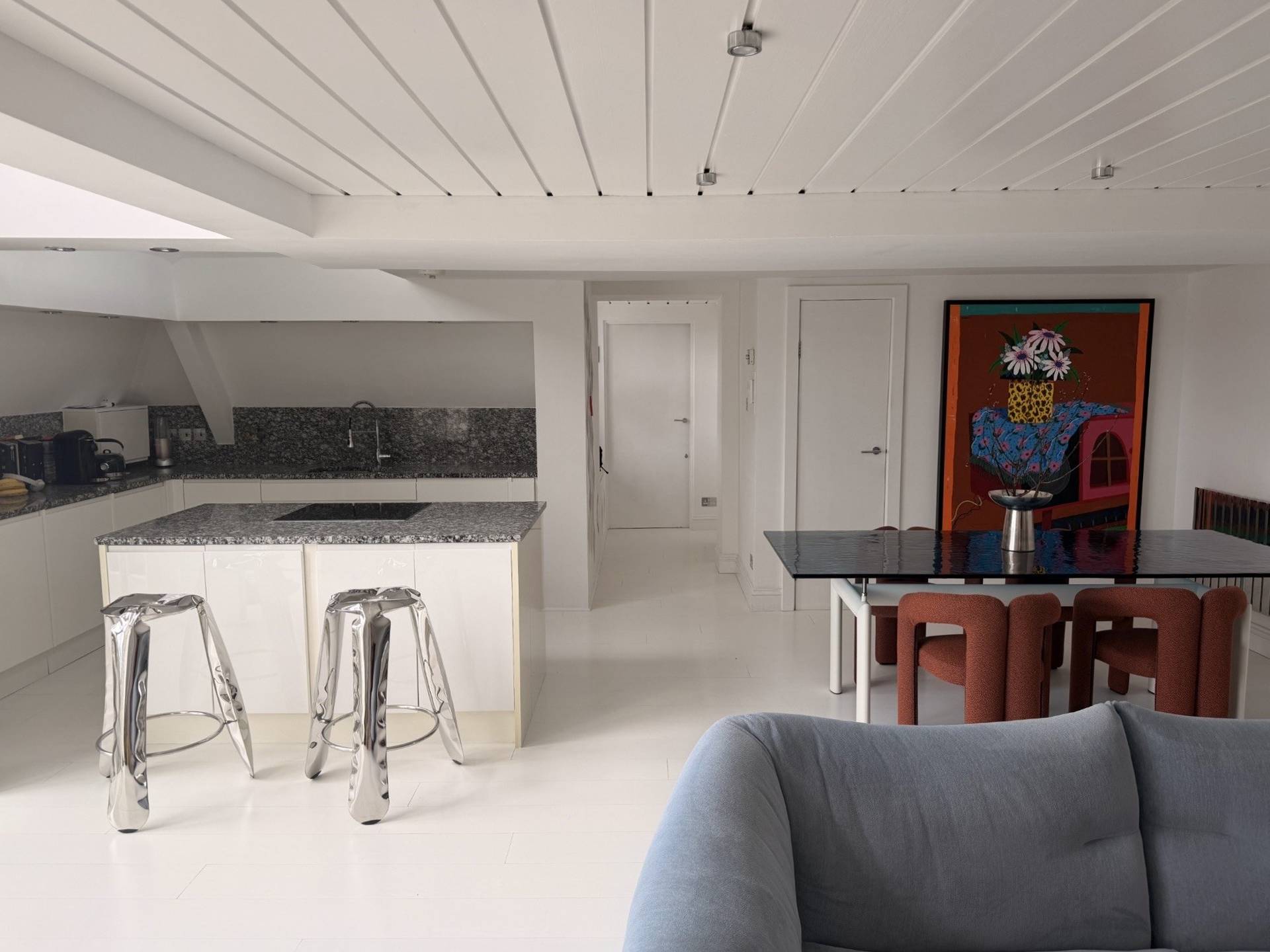 Modern white kitchen and dining space in a Brixton SW4 converted school loft available via Love Locations, showcasing a white kitchen island, chrome bar stools, and crisp white ceilings.