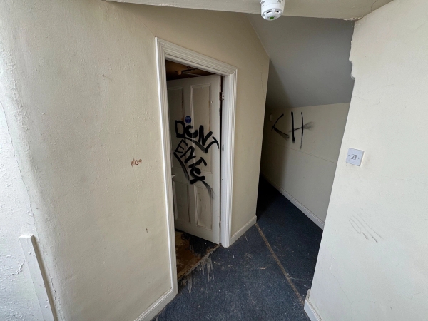 Dark, atmospheric interior doorway with scrawled graffiti tags inside an abandoned mansion outbuilding, via Love Locations.
