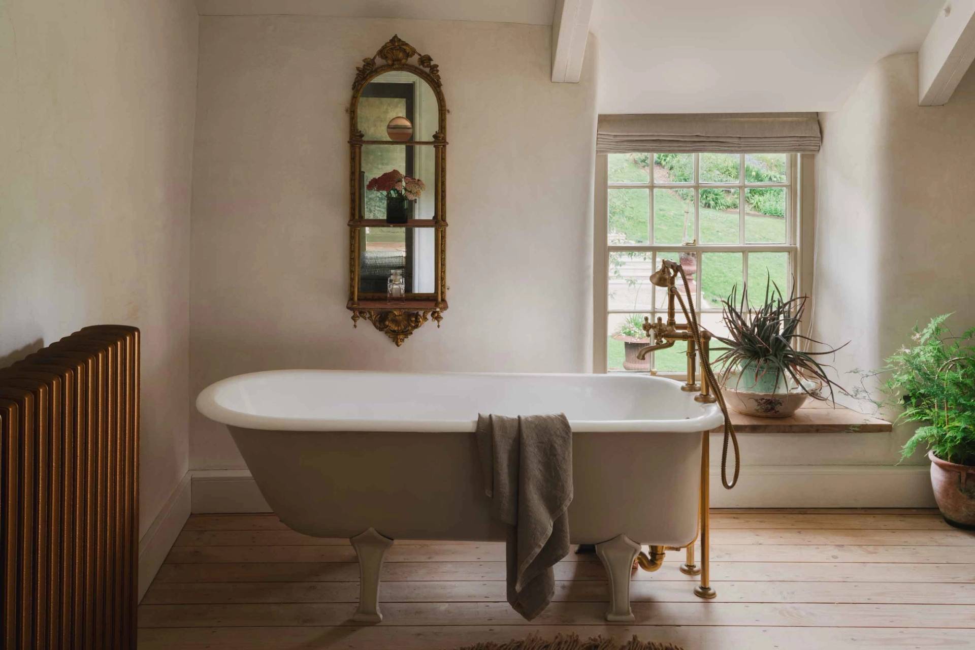 Freestanding roll-top bathtub set beneath a bright window in a Grade II-listed Newquay manor bathroom through Love Locations.
