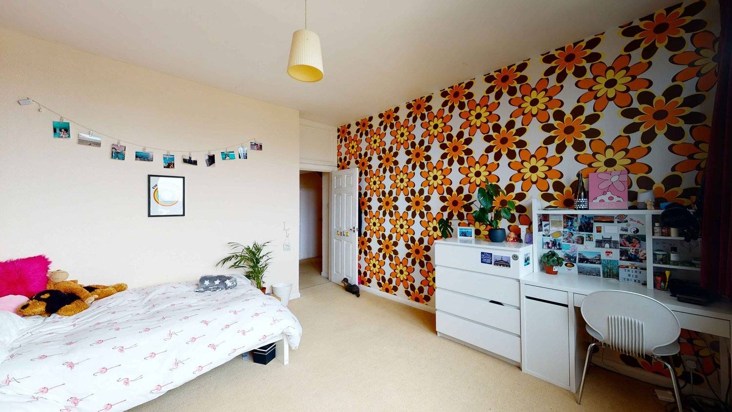 Vintage bedroom with bright orange and brown flower-power wallpaper, white dresser, and neutral carpet, Love Locations SW16.