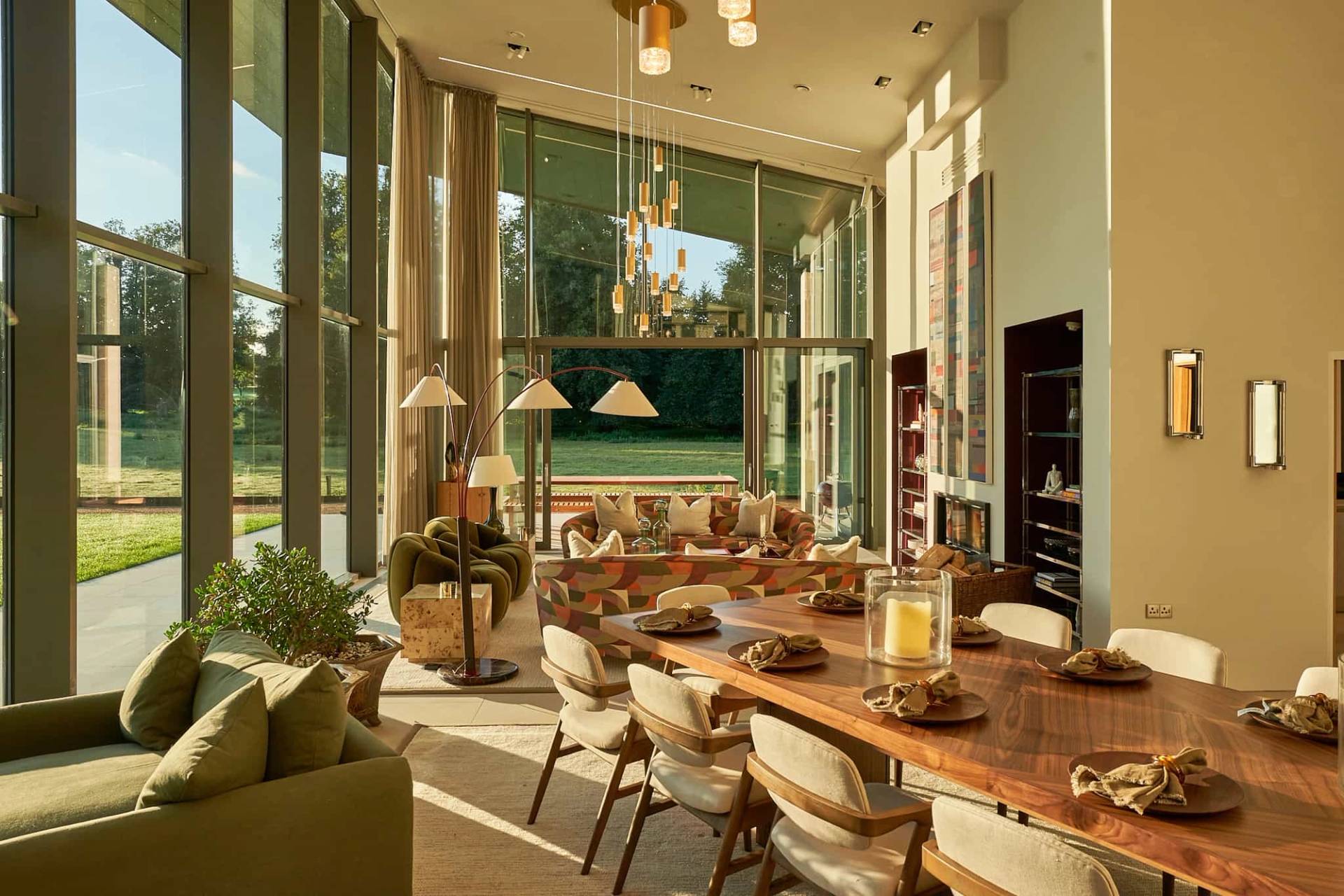 Double-height glass dining room with a long solid timber table, contemporary chairs, and garden views in Winchester, Love Locations SO21.
