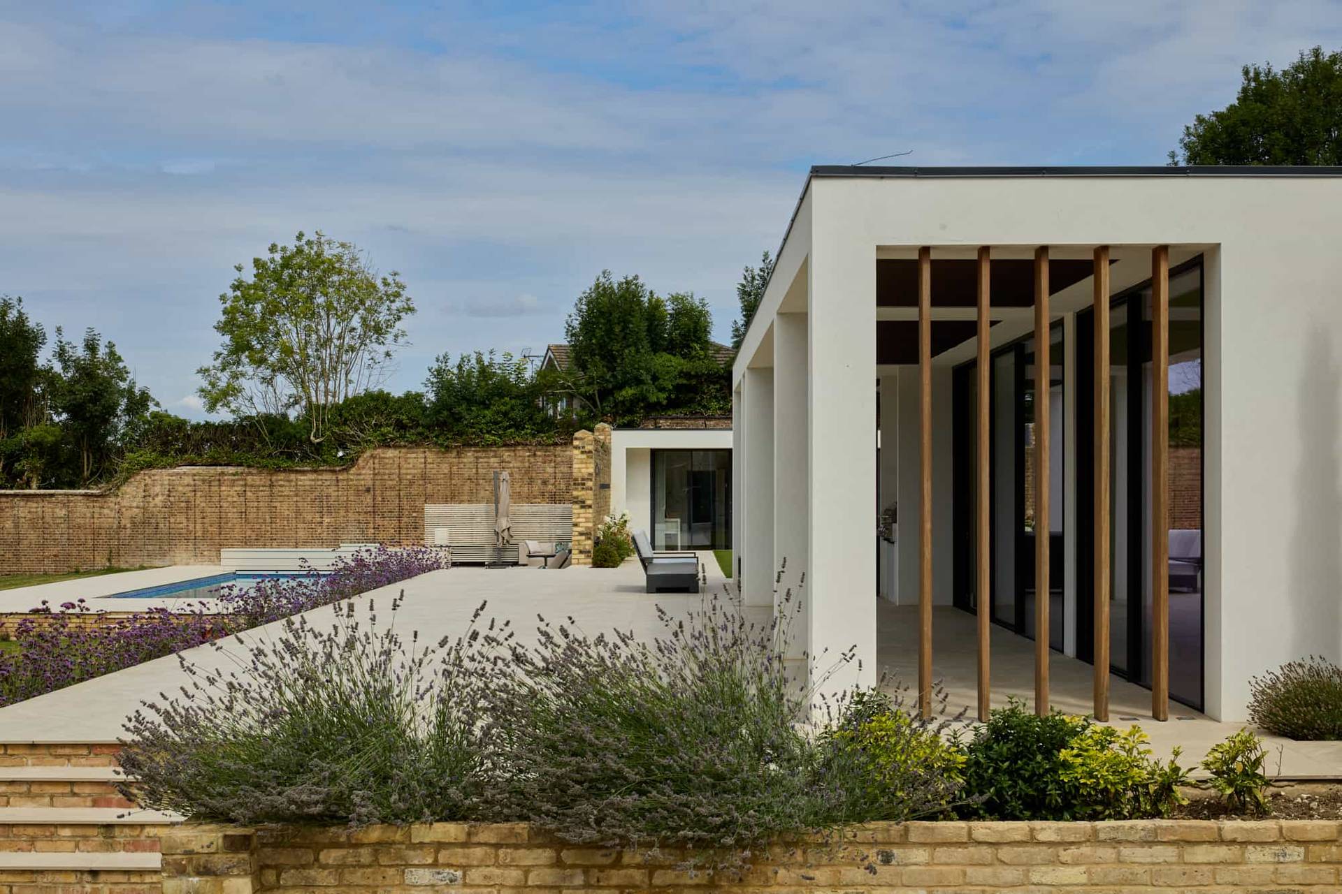 Side elevation of a modern villa showcasing timber slatted screens, yellow brick walls, and paved garden pathways, Love Locations KT22.