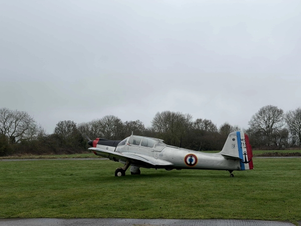 Vintage silver airplane stationed on a historic airfield grass runway, ideal for aviation magazine fashion lookbooks, Love Locations.
