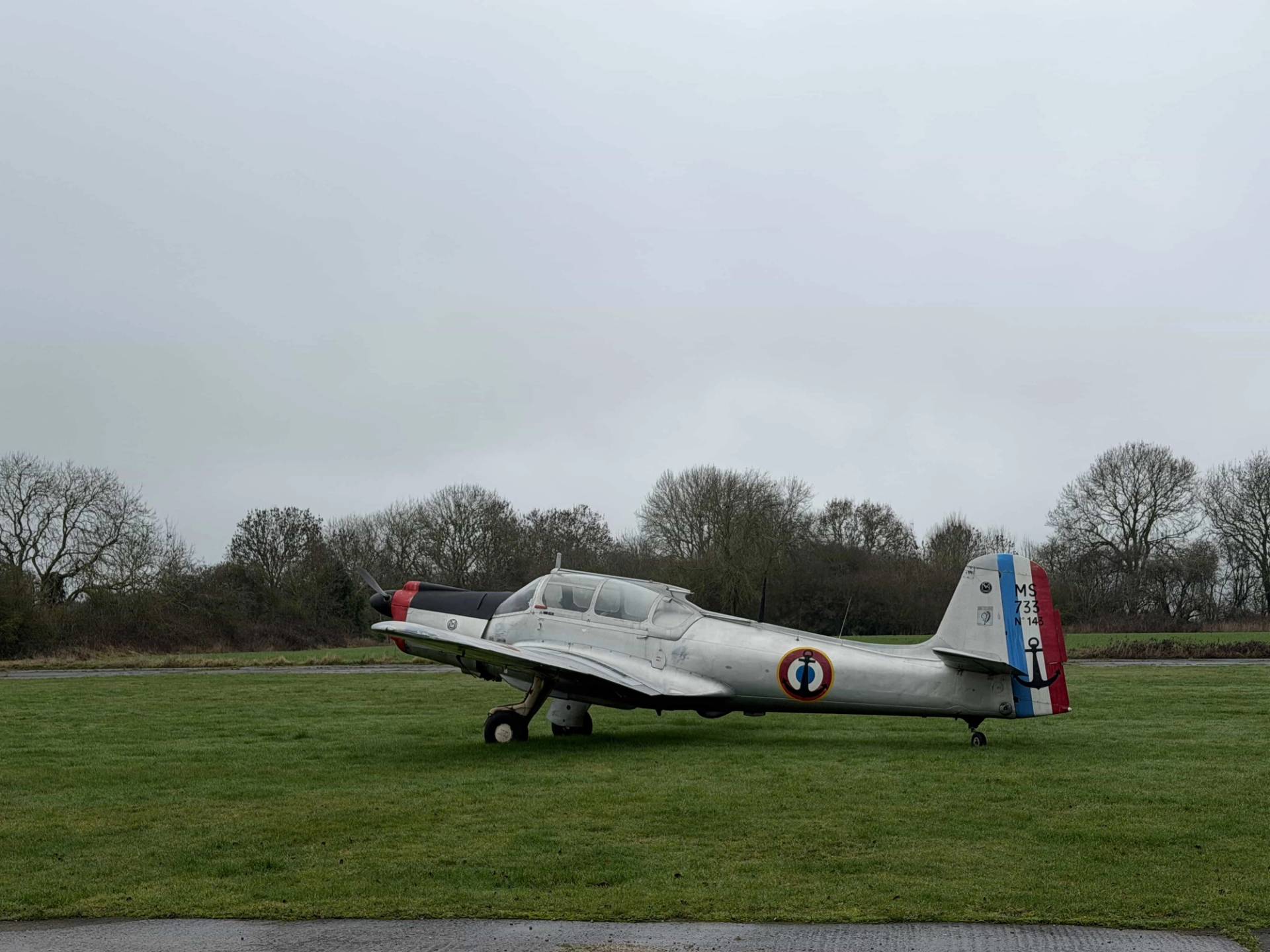Vintage silver airplane stationed on a historic airfield grass runway, ideal for aviation magazine fashion lookbooks, Love Locations.