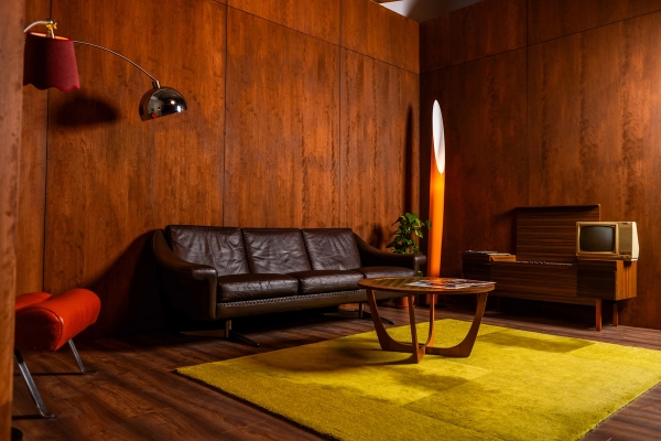 Mid-century modern lounge set with dark wood wall panelling, black leather sofa, chartreuse rug, and retro lighting, Love Locations N15.