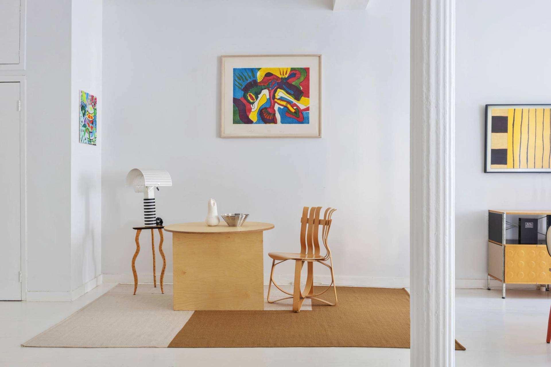 Minimalist wooden writing desk and bentwood chair nook in a bright Tribeca artist loft photoshoot venue by Love Locations, featuring framed colorful artwork on clean white walls.