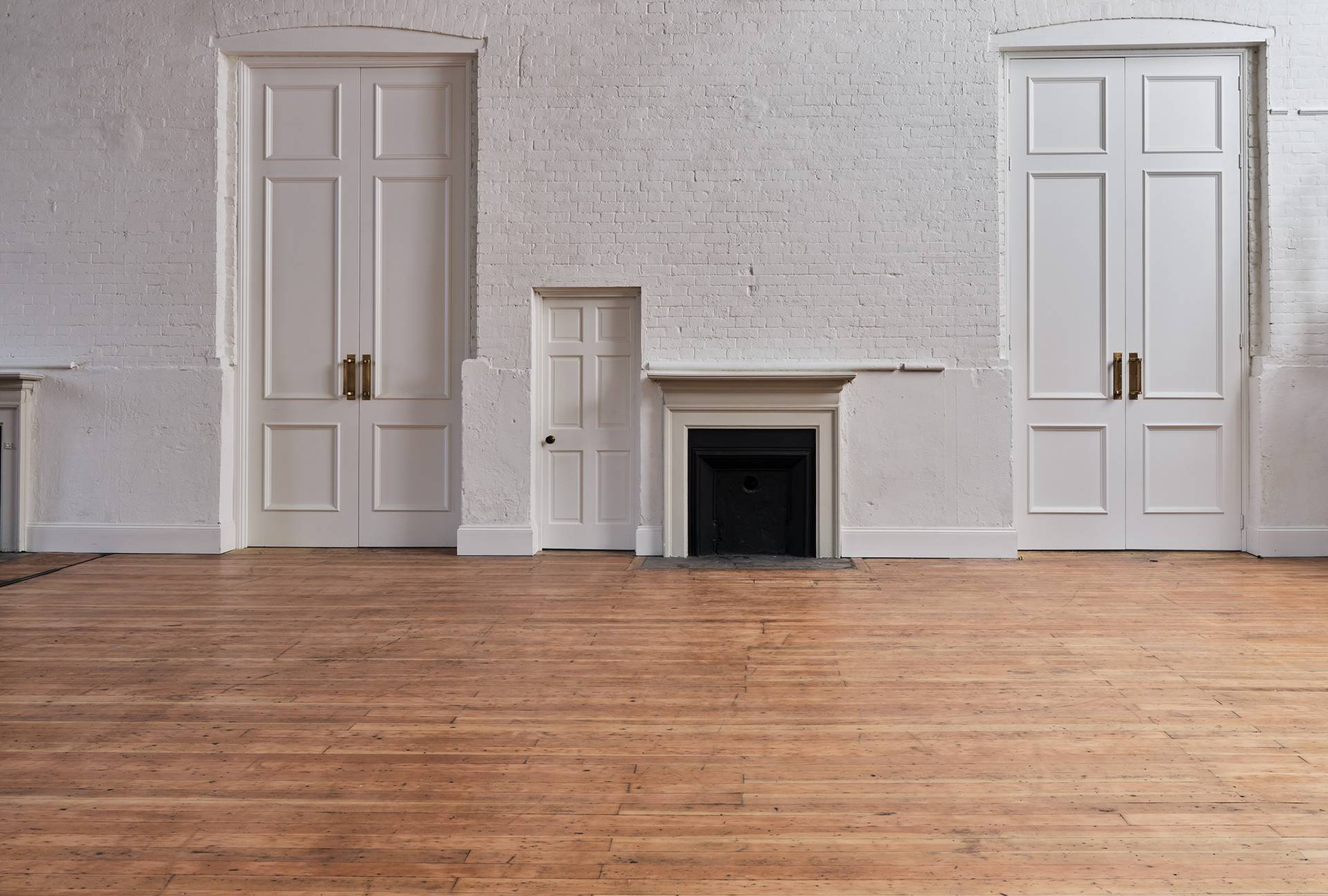 White panelled hall wall featuring a dark fireplace hearth and white double doors, Love Locations.