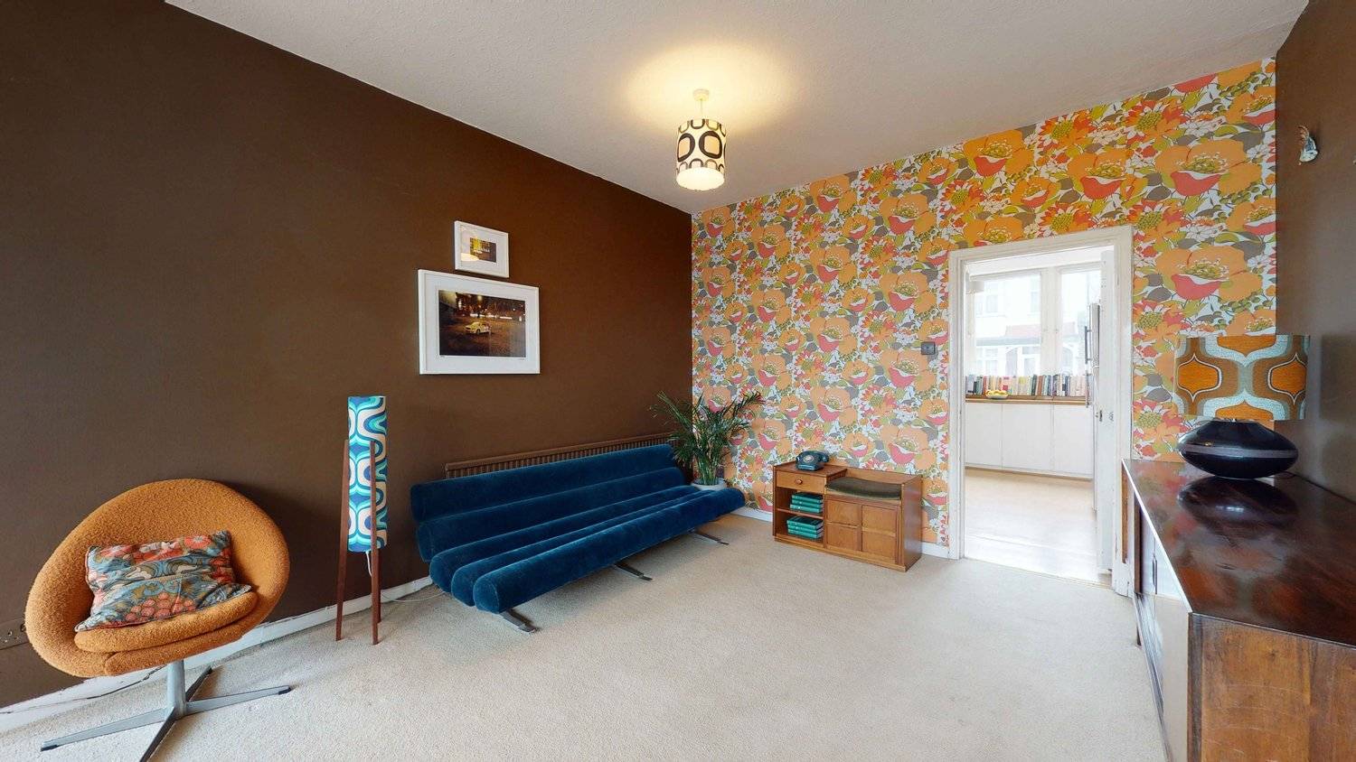 Vintage living space featuring a deep blue velvet sofa, floral 70s wallpaper, and mid-century wooden sideboard, Love Locations SW16.