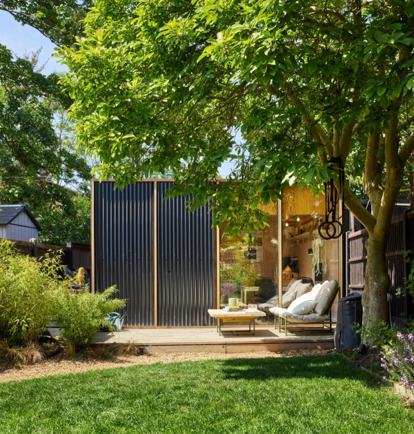 Modern clad garden studio pod set beneath a mature shade tree on a suburban lawn, Love Locations E17.
