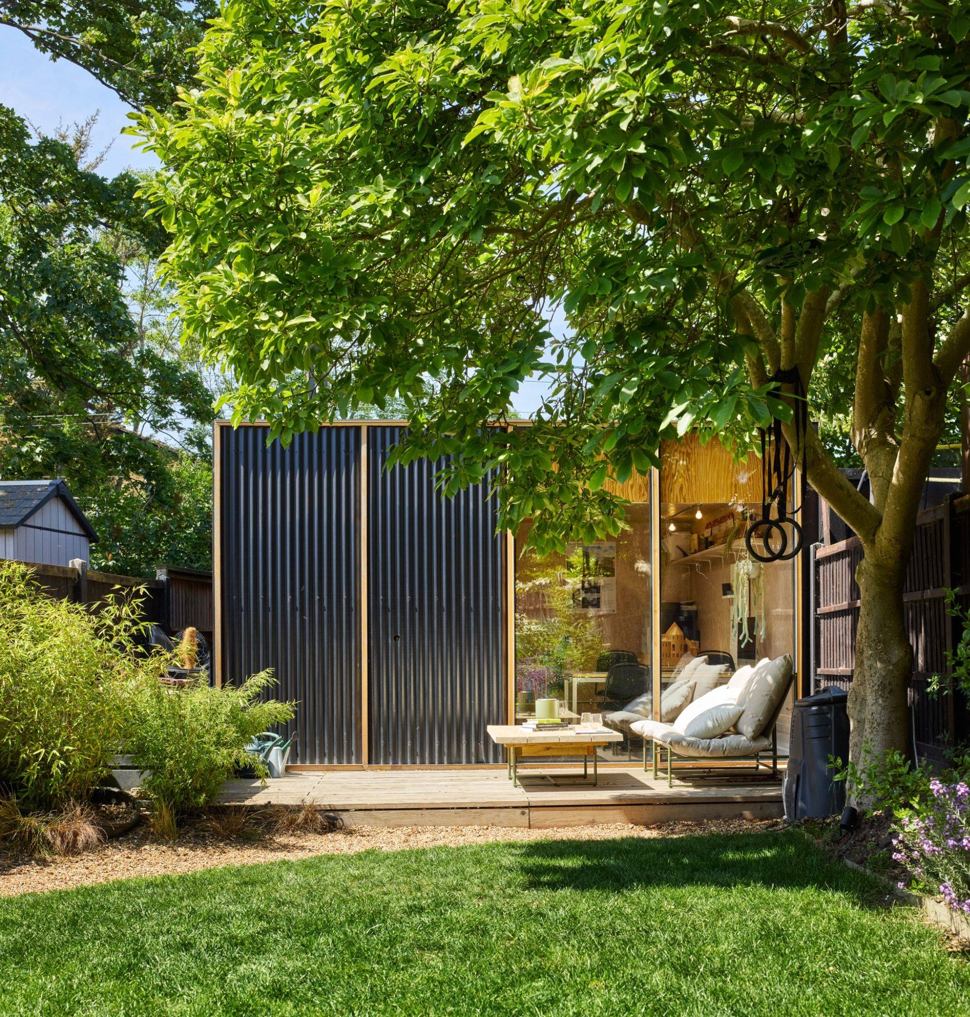 Modern clad garden studio pod set beneath a mature shade tree on a suburban lawn, Love Locations E17.