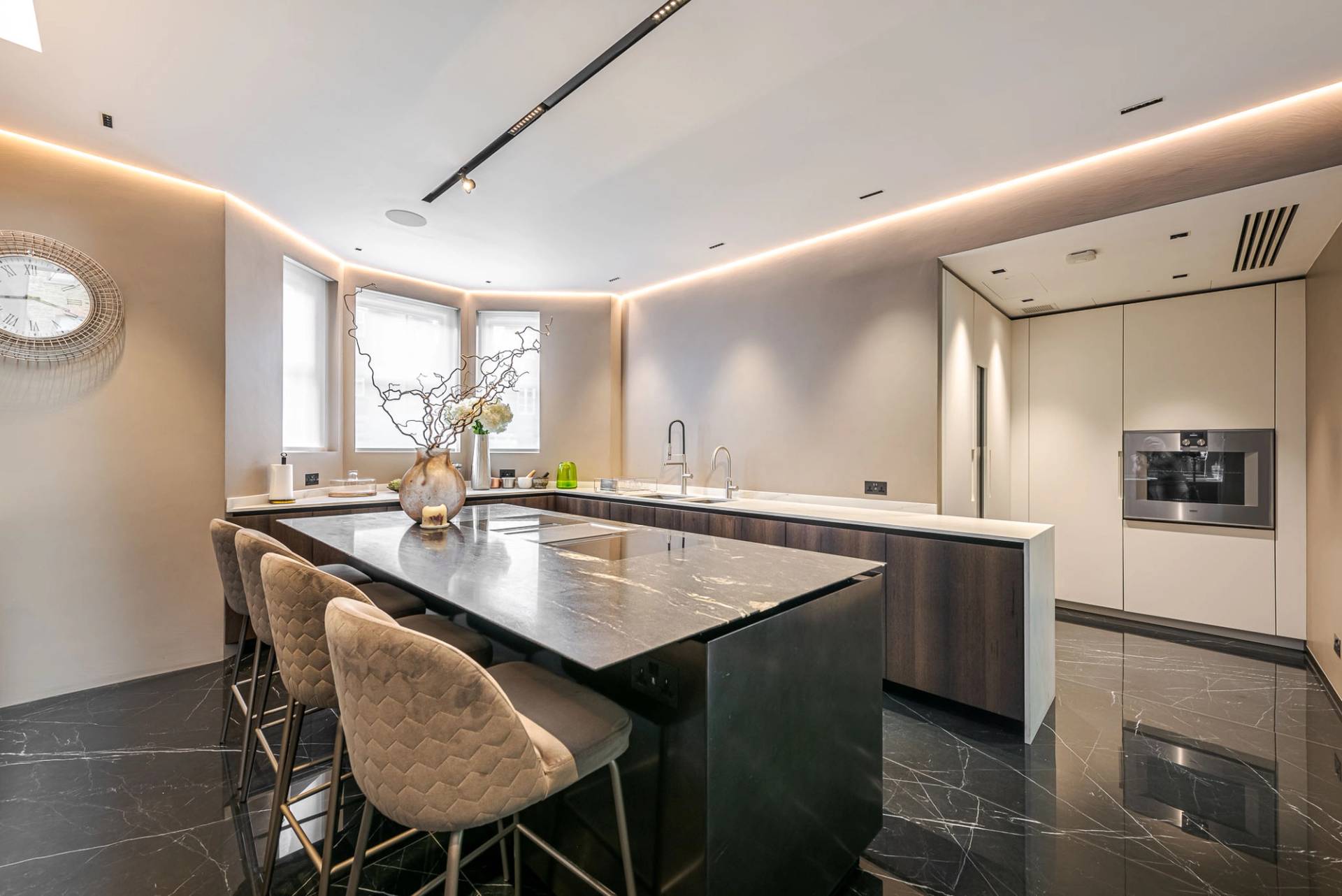 Kitchen island unit featuring high upholstered bar chairs set against dark marble walls, Love Locations SW11.