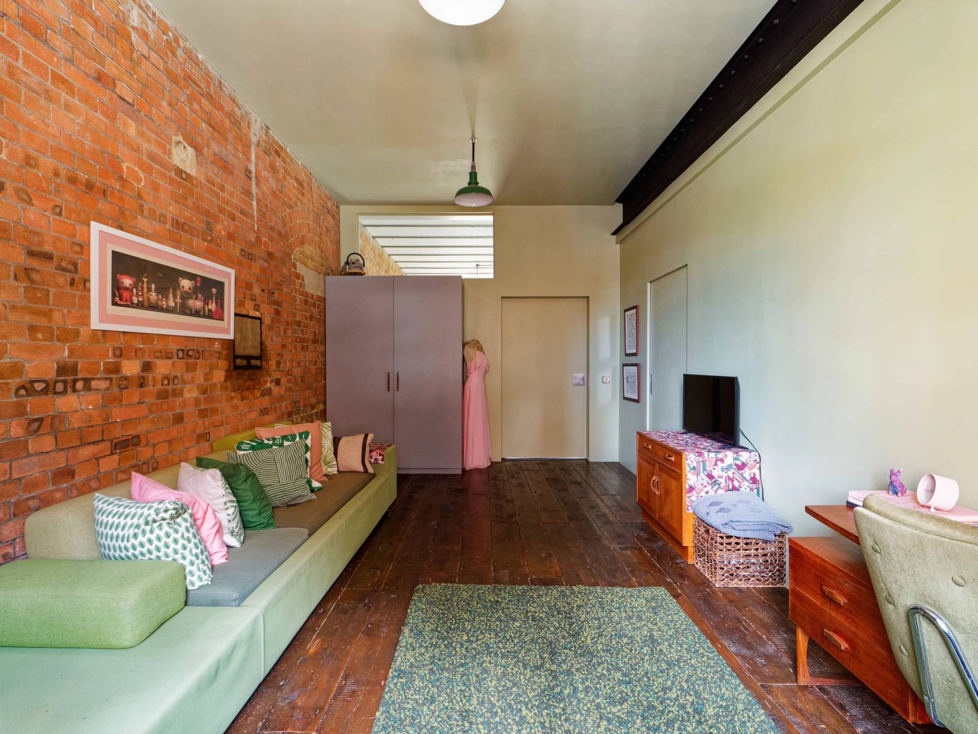 Casual loft lounge area with green sofa, wooden floors, exposed brickwork, and low-profile storage cabinets, Love Locations E14.