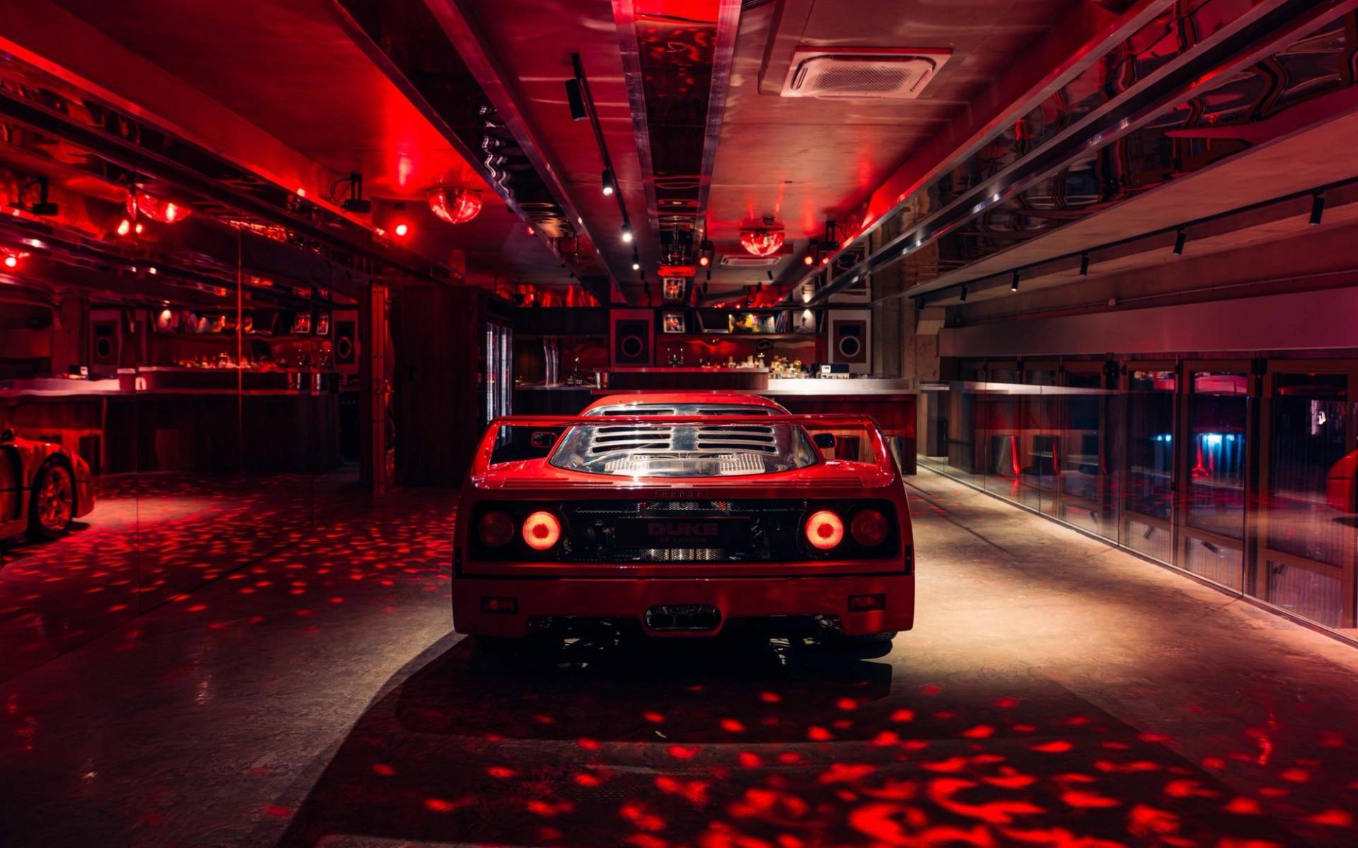 Classic red Ferrari F40 parked under red disco spot lighting in a supercar event venue from Love Locations.