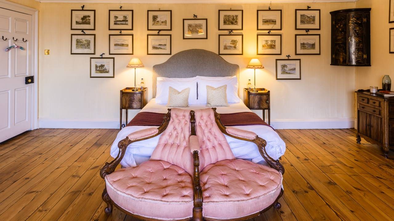 Spacious bedroom suite with twin pink velvet shell armchairs set at the foot of a king bed, Love Locations KY15.