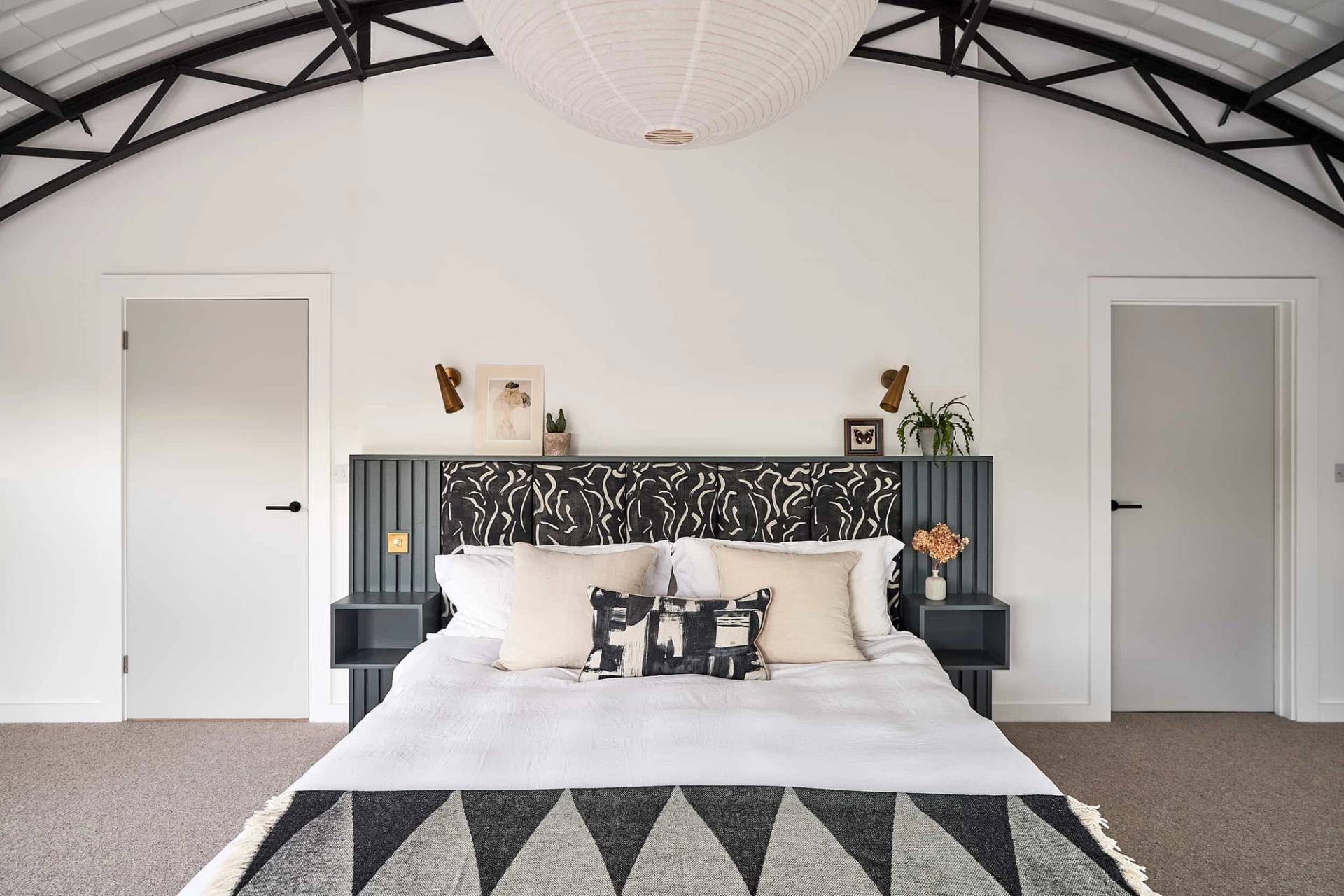 Monochrome master bedroom suite featuring a black and white patterned headboard, triangular rug, and corrugated roof ceiling, Love Locations IP30.