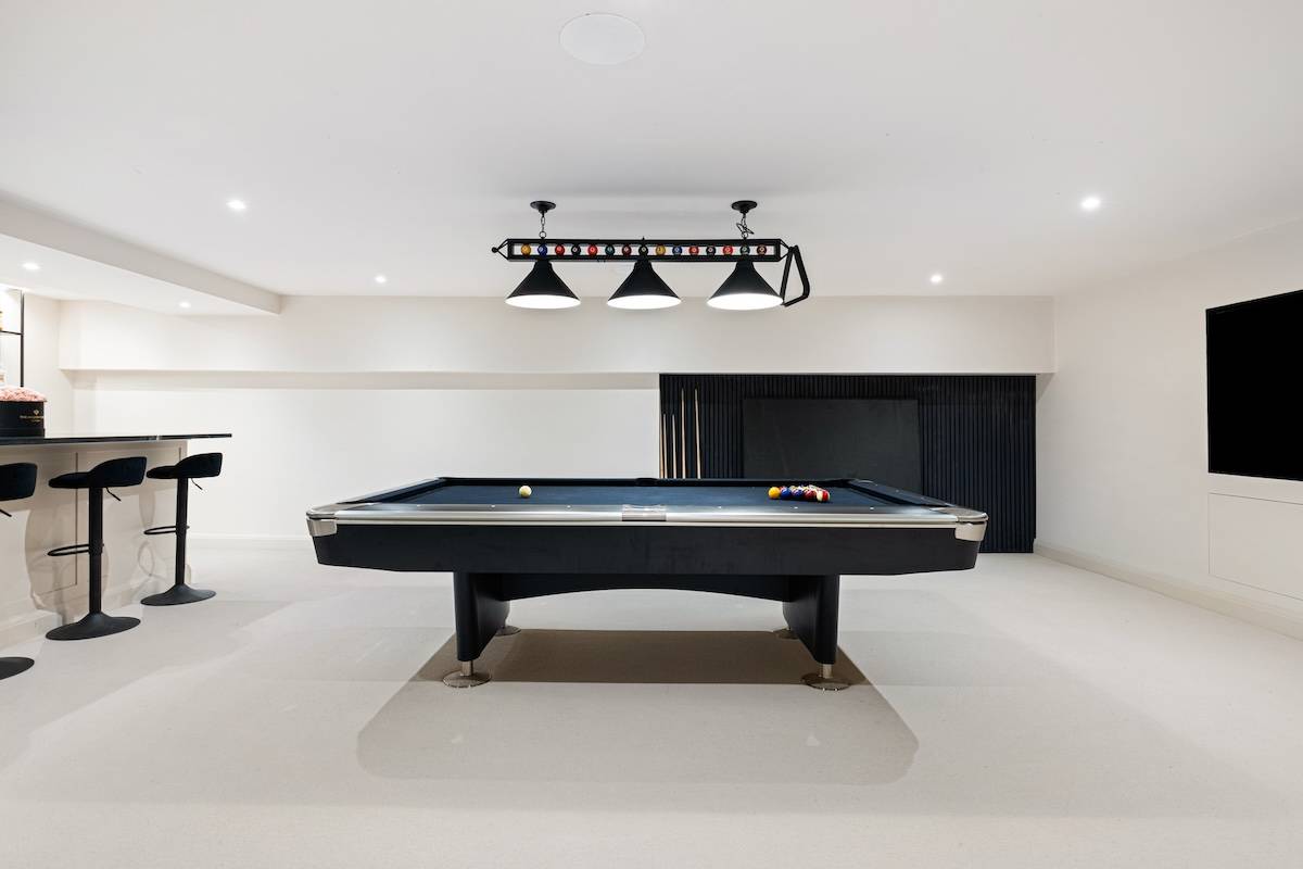 Full-size pool table set in a subterranean entertainment room with black overhead light fixtures, Love Locations RH13.