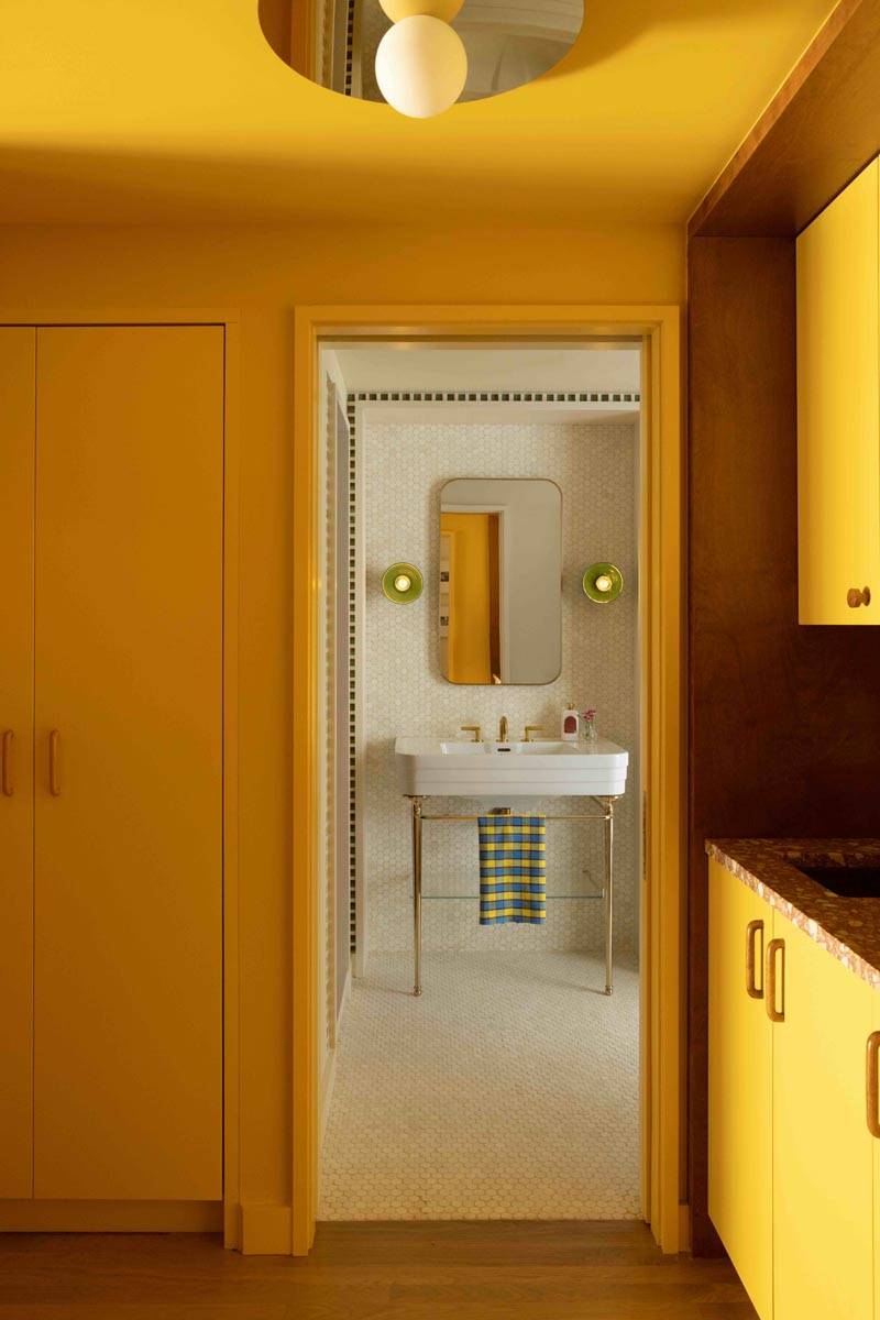 Warm ochre-painted bathroom photoshoot location in Boerum Hill Brooklyn through Love Locations, featuring a white wall-hung sink and mirror view into an adjoining room.