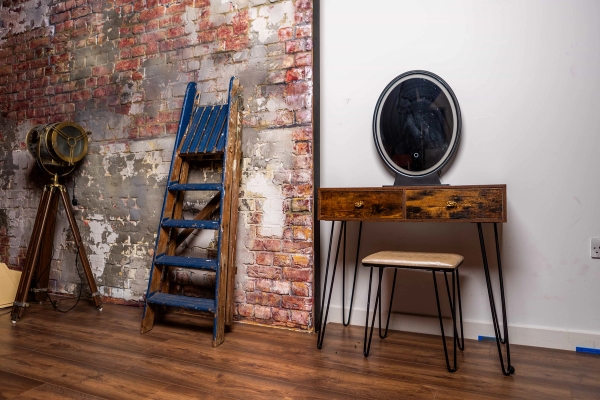 Makeup dressing set with a rustic wooden vanity table, oval mirror, blue ladder, and exposed brick backdrop, Love Locations N15.