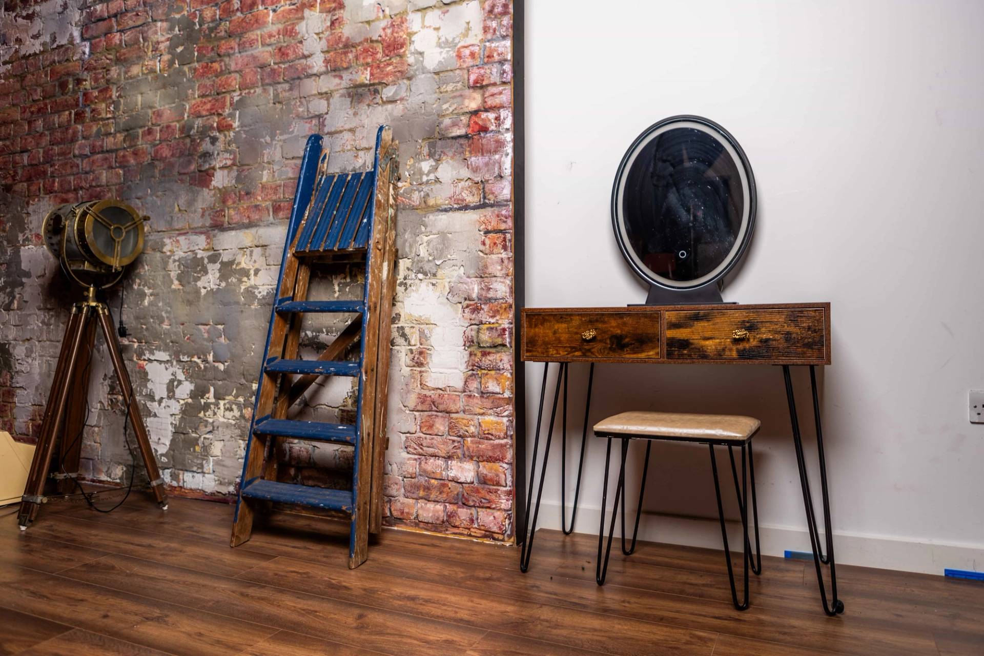 Makeup dressing set with a rustic wooden vanity table, oval mirror, blue ladder, and exposed brick backdrop, Love Locations N15.