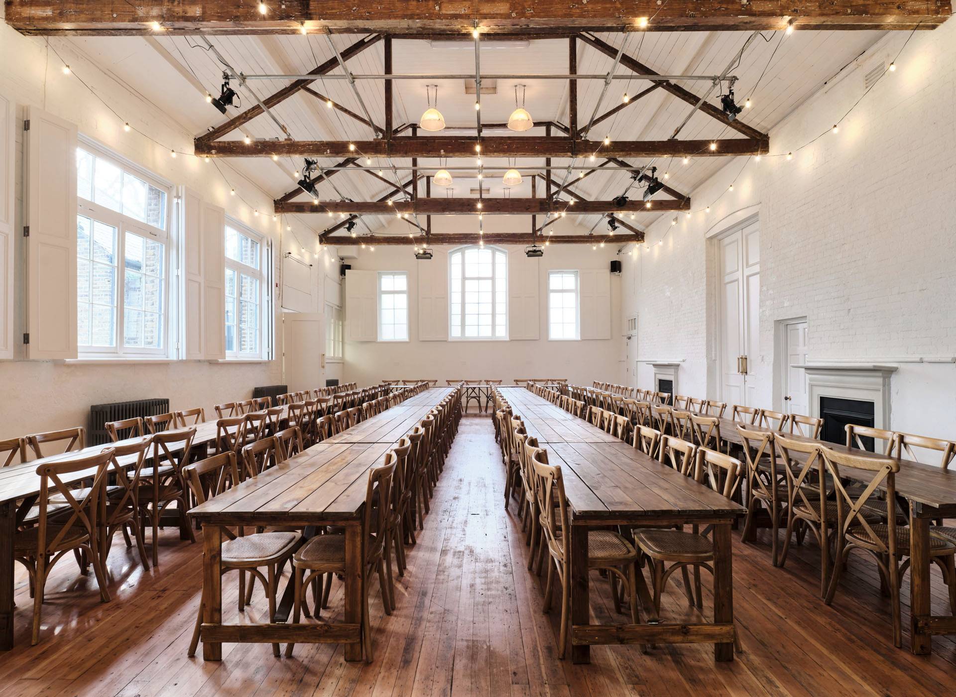 Banqueting layout setup in a vaulted Shoreditch hall venue featuring long wooden tables and cross-back chairs, ideal for weddings and private dining events, Love Locations.