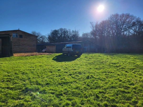 Sunlit grassy farm field with timber outbuilding and parked off-road vehicle in South Chailey, Love Locations BN8.