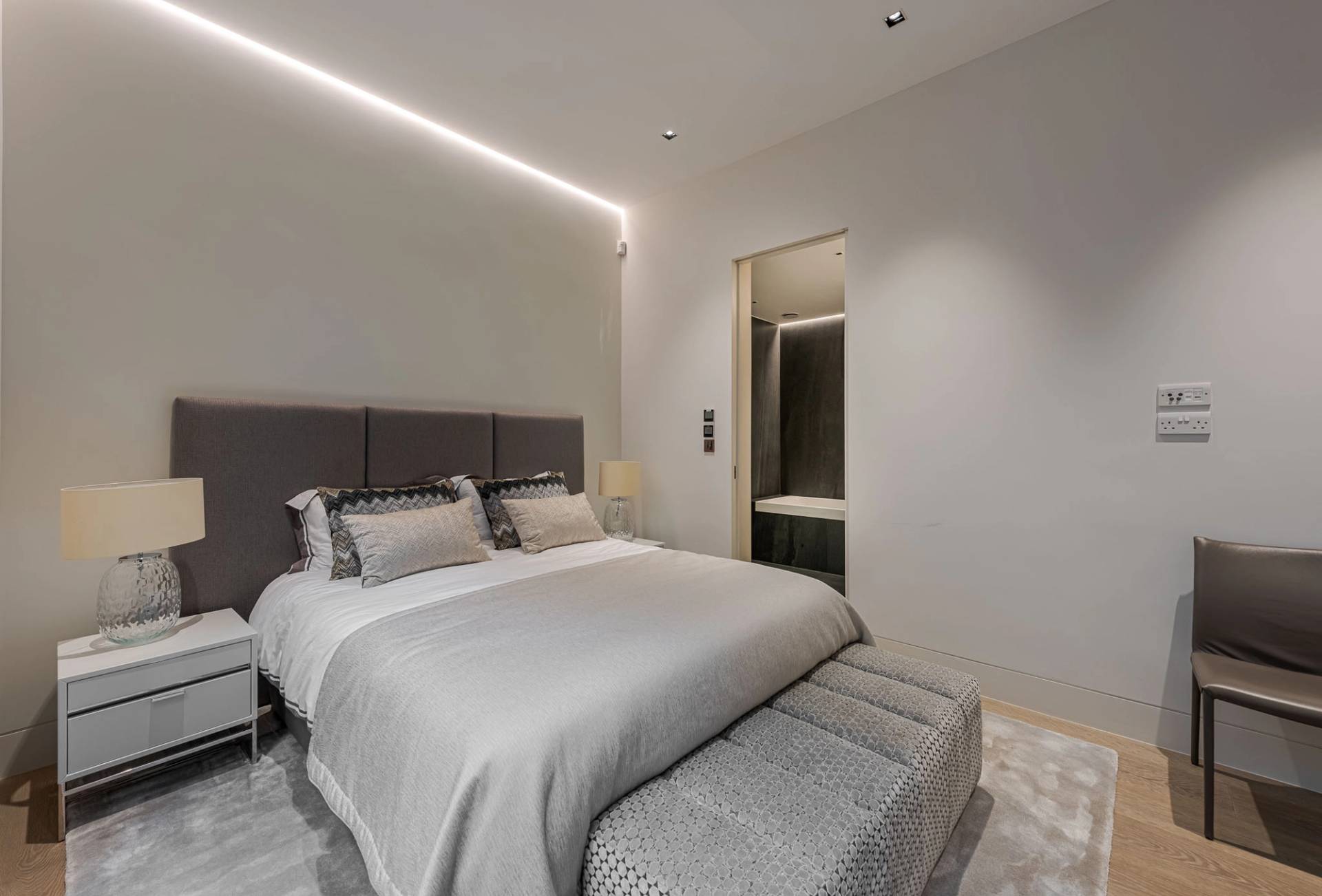 Guest bedroom suite with grey upholstered headboard, footstool bench, and LED ambient strip lighting, Love Locations SW11.