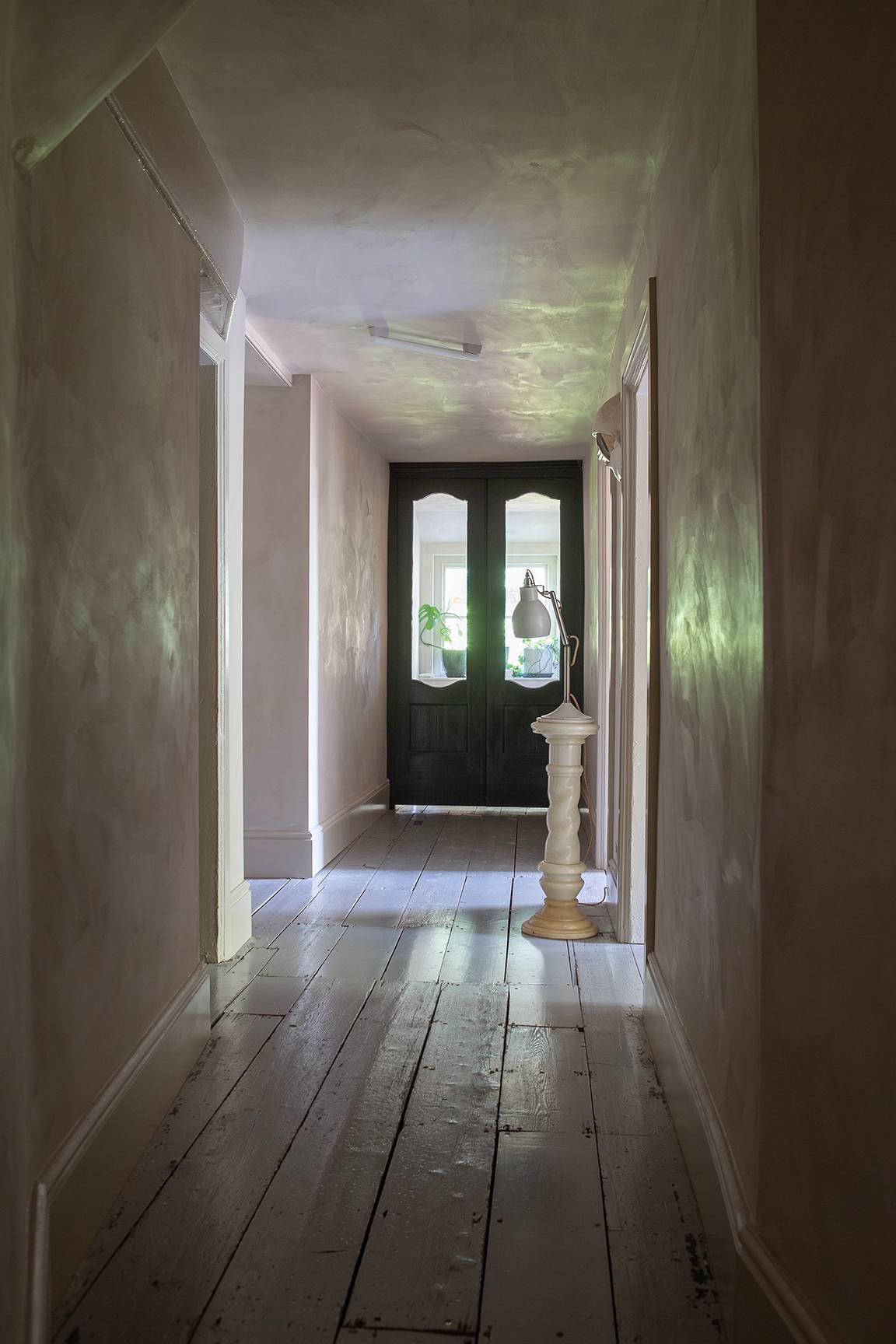 Long white hallway corridor with wood floorboards, framed artwork, and dark exit door, Love Locations ME13.