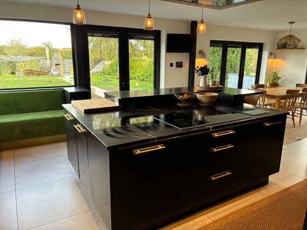 High-end luxury kitchen shoot location in Essex CM4 through Love Locations, featuring a massive dark central island with built-in cooktop, pendant lighting, and surrounding glass windows.