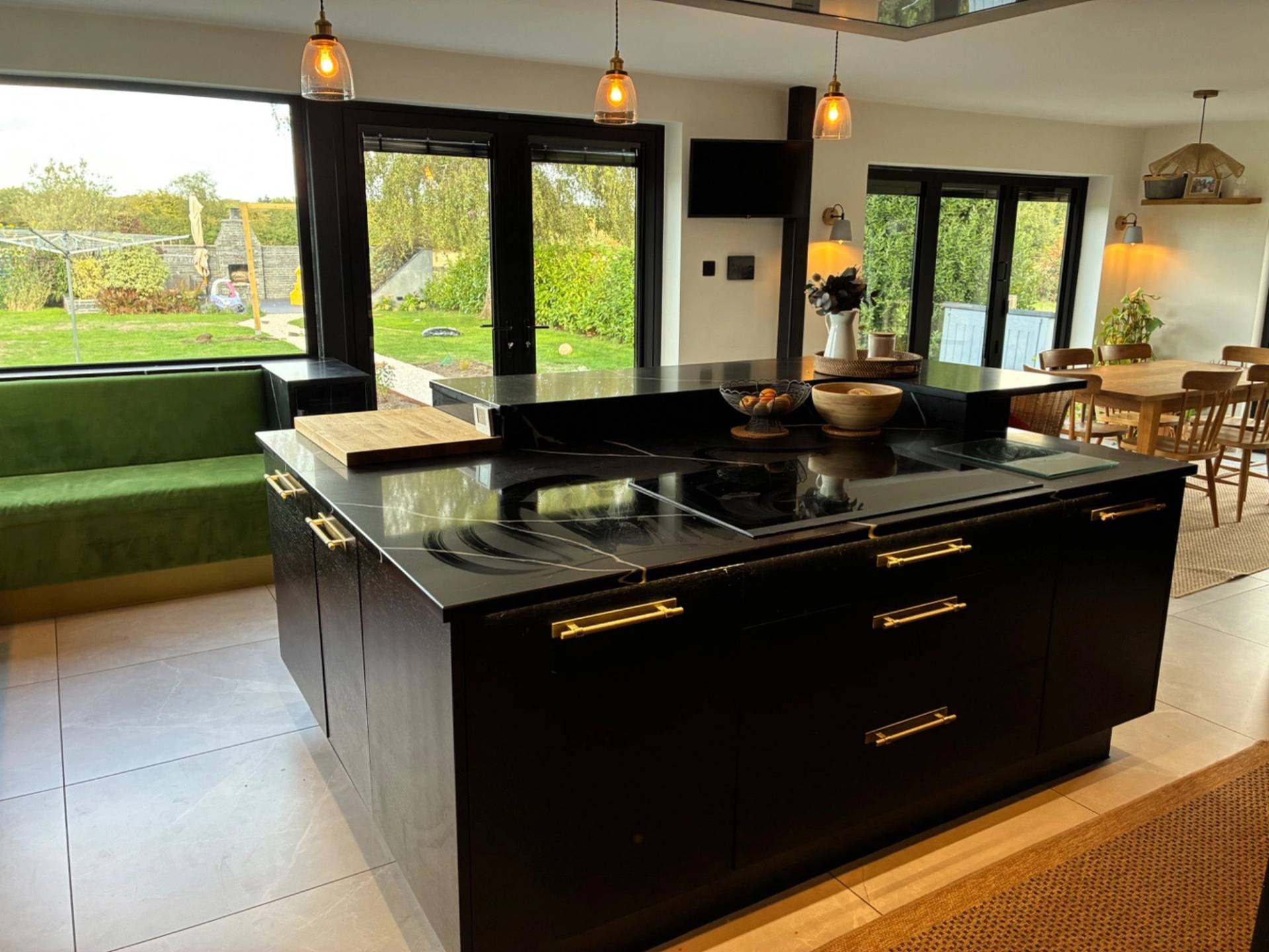 High-end luxury kitchen shoot location in Essex CM4 through Love Locations, featuring a massive dark central island with built-in cooktop, pendant lighting, and surrounding glass windows.