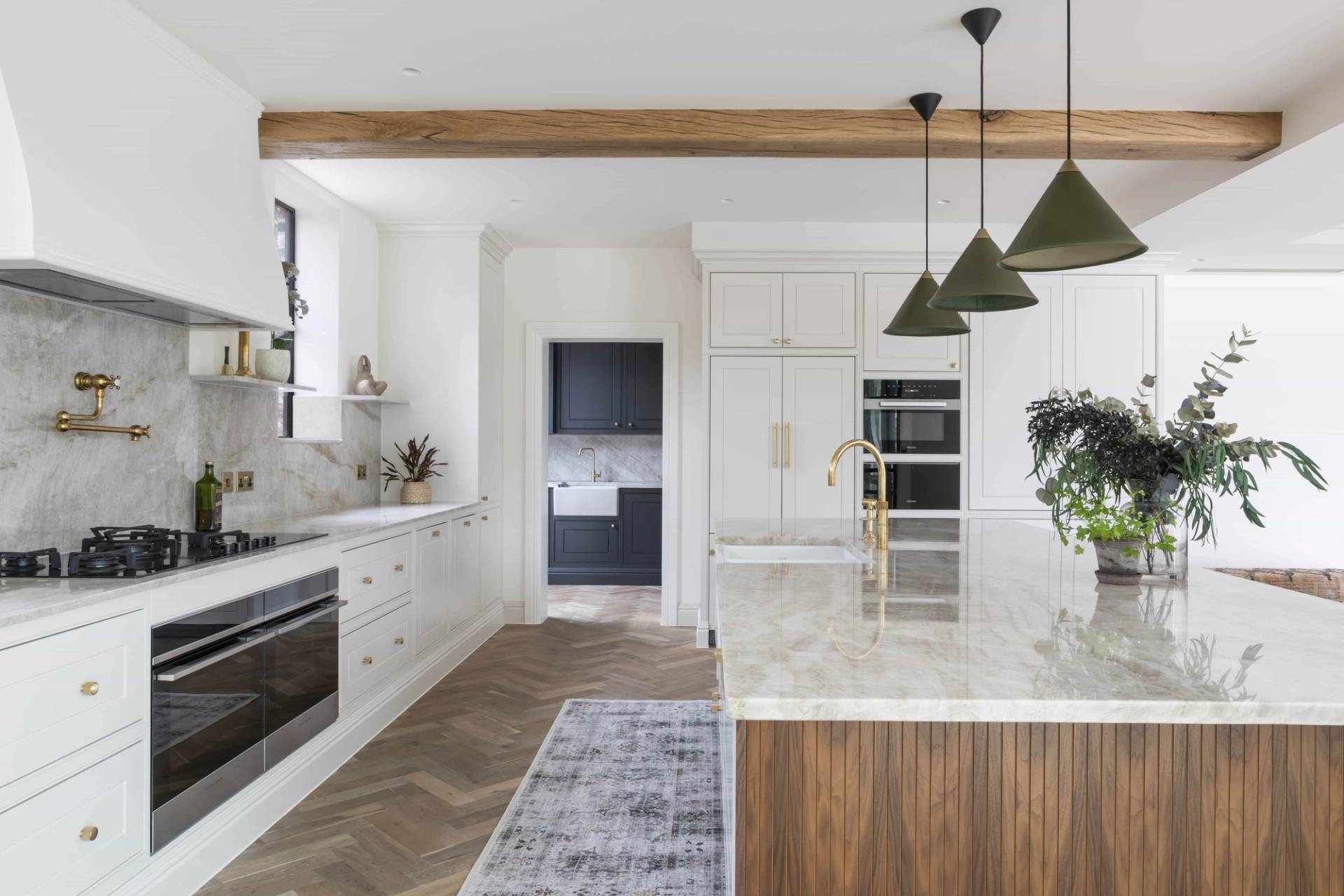 Bright white kitchen in HP18 with exposed timber beams, marble countertops, runner rug, and open-plan layout, Love Locations Buckinghamshire.