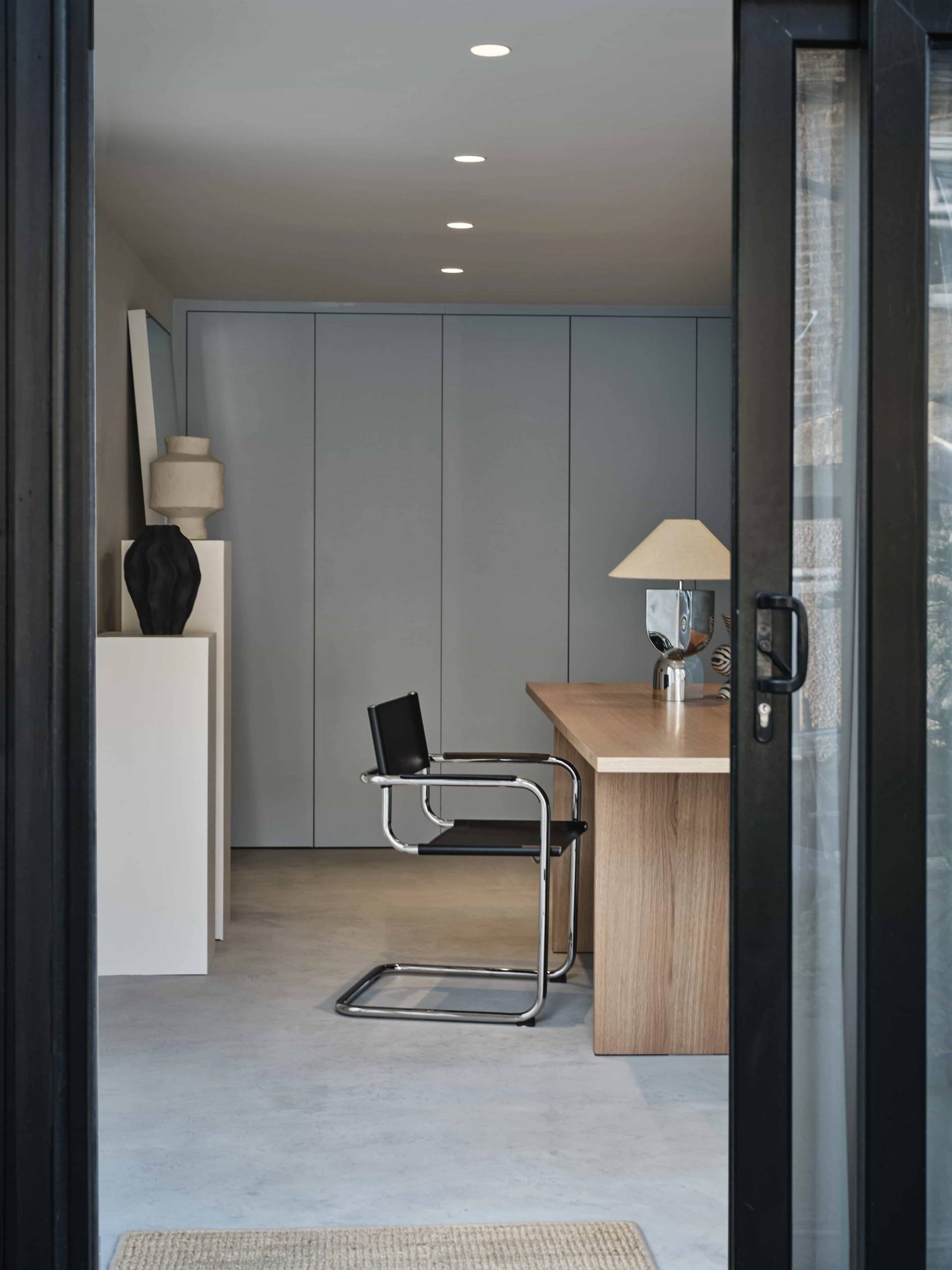 Interior view of a garden office studio featuring a light oak desk, black office chair, and powder blue fitted wardrobes, Love Locations E4.