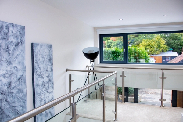 Open mezzanine landing area featuring modern glass railings and architectural spotlighting, premium residential shoot space via Love Locations.