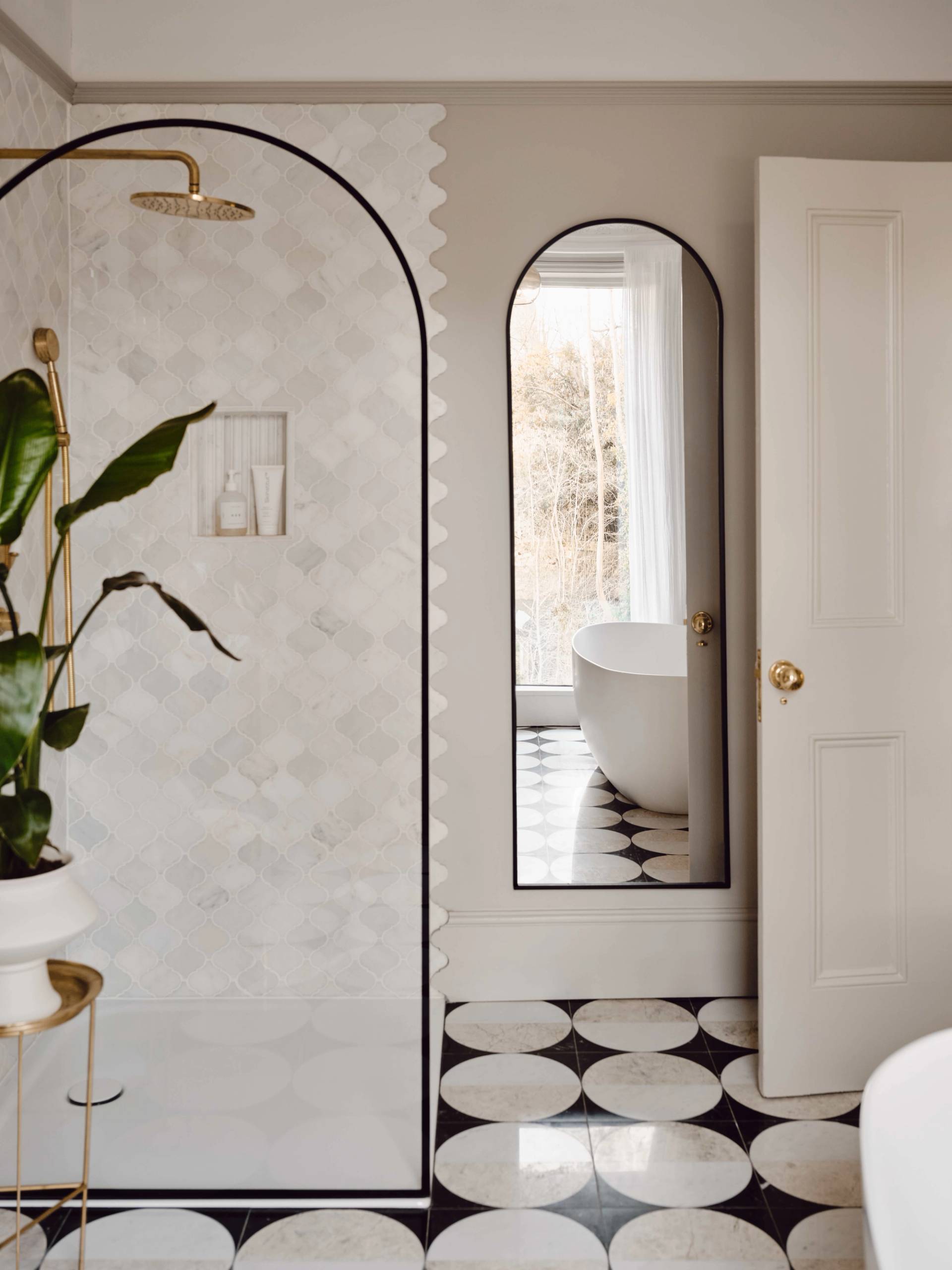 Luxury ensuite bathroom featuring arched mirrors, freestanding white soaking tub, and black and white checkerboard tile floor, Love Locations CR0.