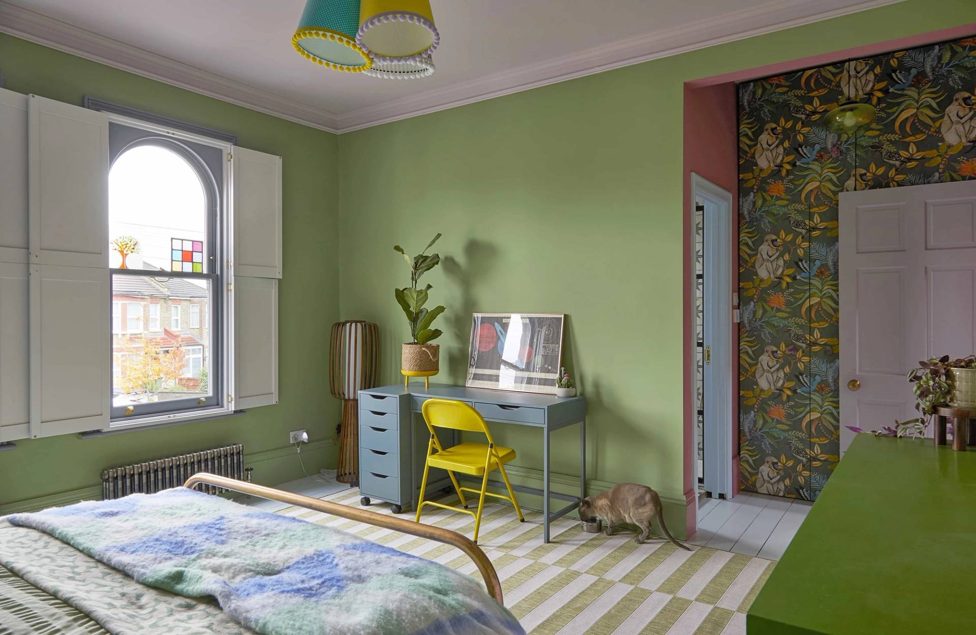 Bright bedroom with pistachio green walls, yellow desk chair, grey writing desk, and striped rug, Love Locations Catford.
