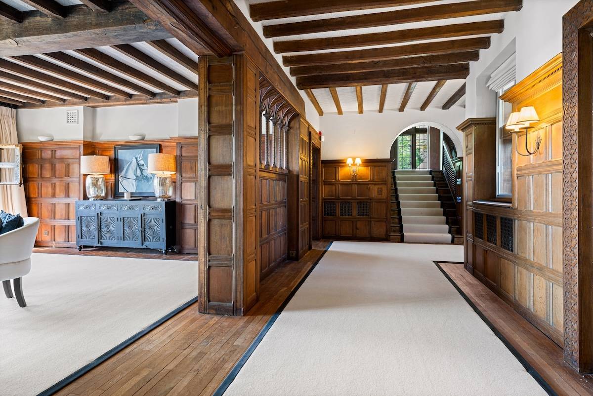 Grand country mansion entrance hallway in Horsham, RH13 featuring dark oak panelling, neutral runner carpet, and grand wooden staircase via Love Locations.