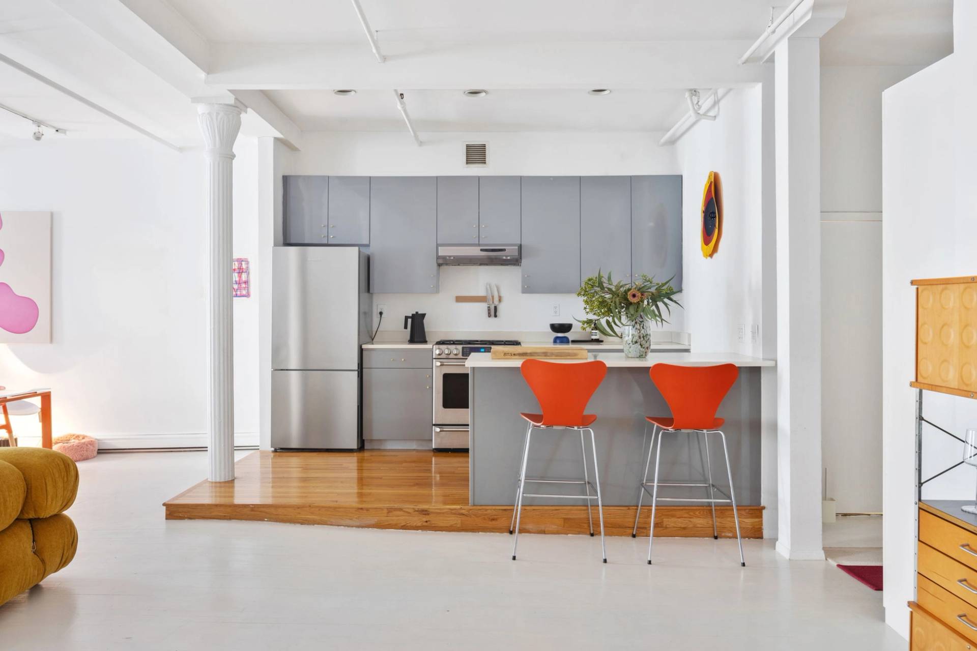Sleek modern grey kitchen and island bar in a Tribeca NYC 10007 loft shoot space through Love Locations, featuring orange counter stools and original hardwood flooring.