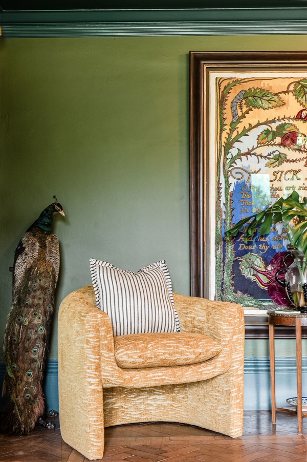 Statement gold armchair positioned next to an exotic peacock prop in a green-walled editorial room layout from Love Locations.