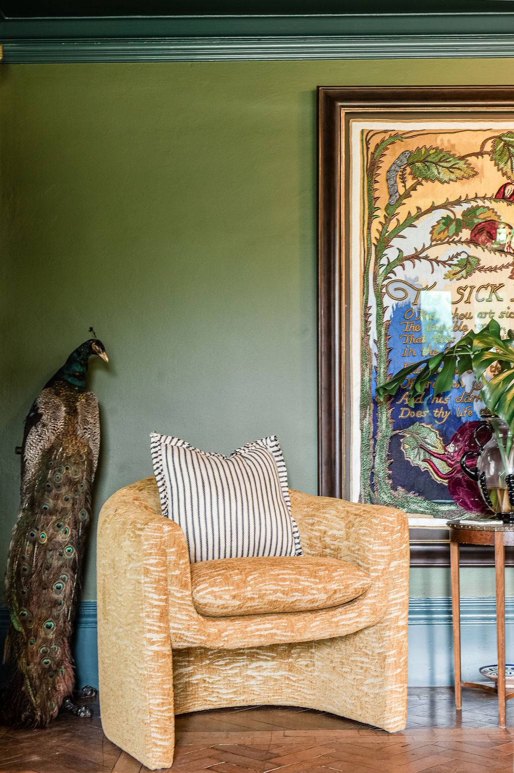 Statement gold armchair positioned next to an exotic peacock prop in a green-walled editorial room layout from Love Locations.