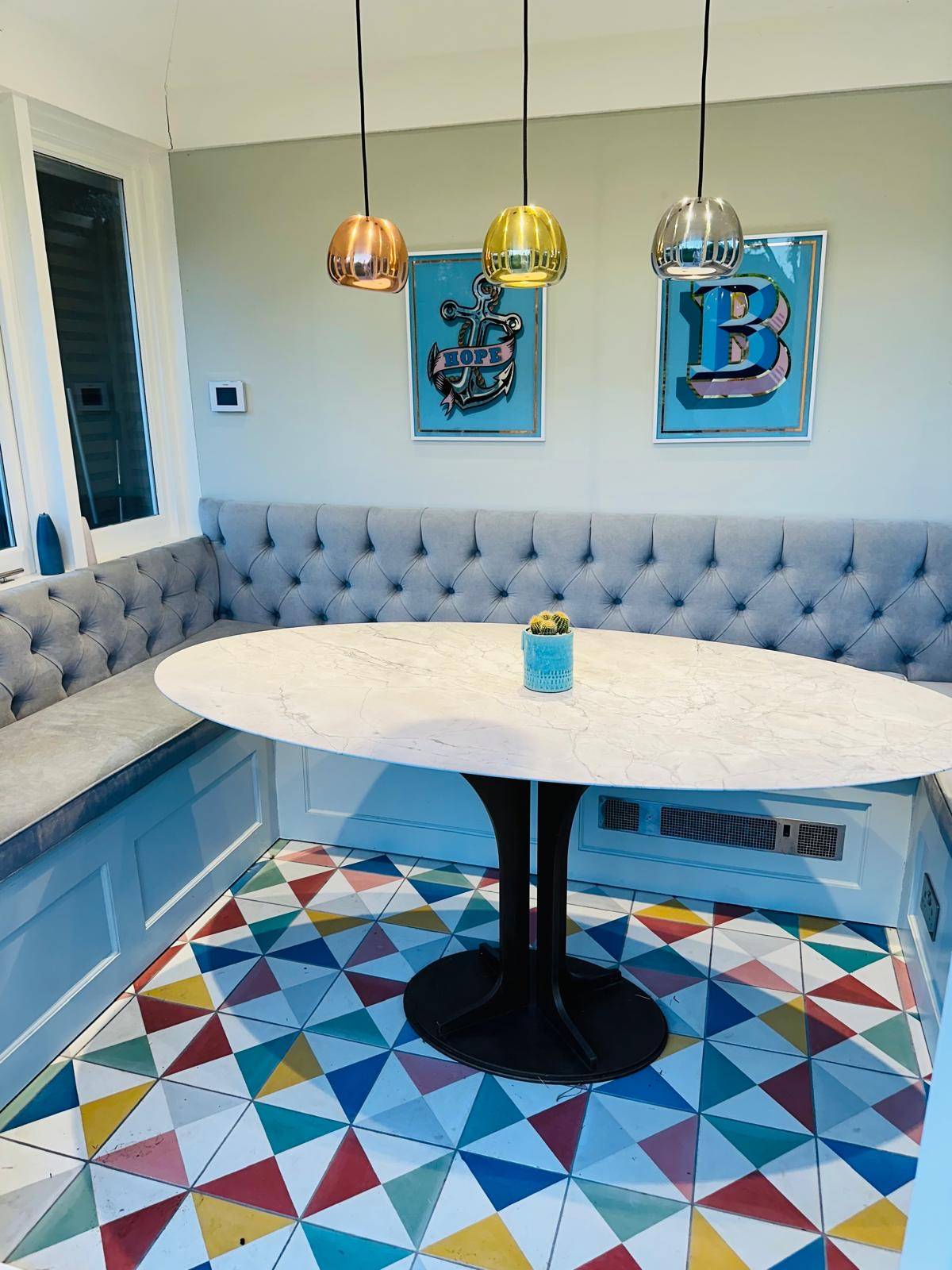 Breakfast nook with blue button-tufted banquette seating, oval table, and patterned floor tiles, Love Locations TW11.