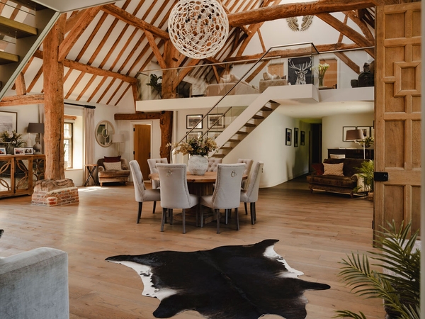 Vaulted double-height barn hall featuring a round wooden dining table, white dining chairs, and cowhide rug, perfect for high-fashion editorial shoots via Love Locations.