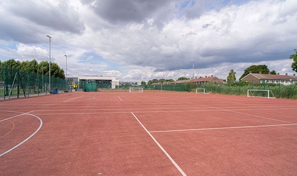 Love Locations hardstanding sports court London SE2: All-weather red outdoor netball and tennis court under a cloudy sky, optimized for athletic apparel campaigns and commercial video.