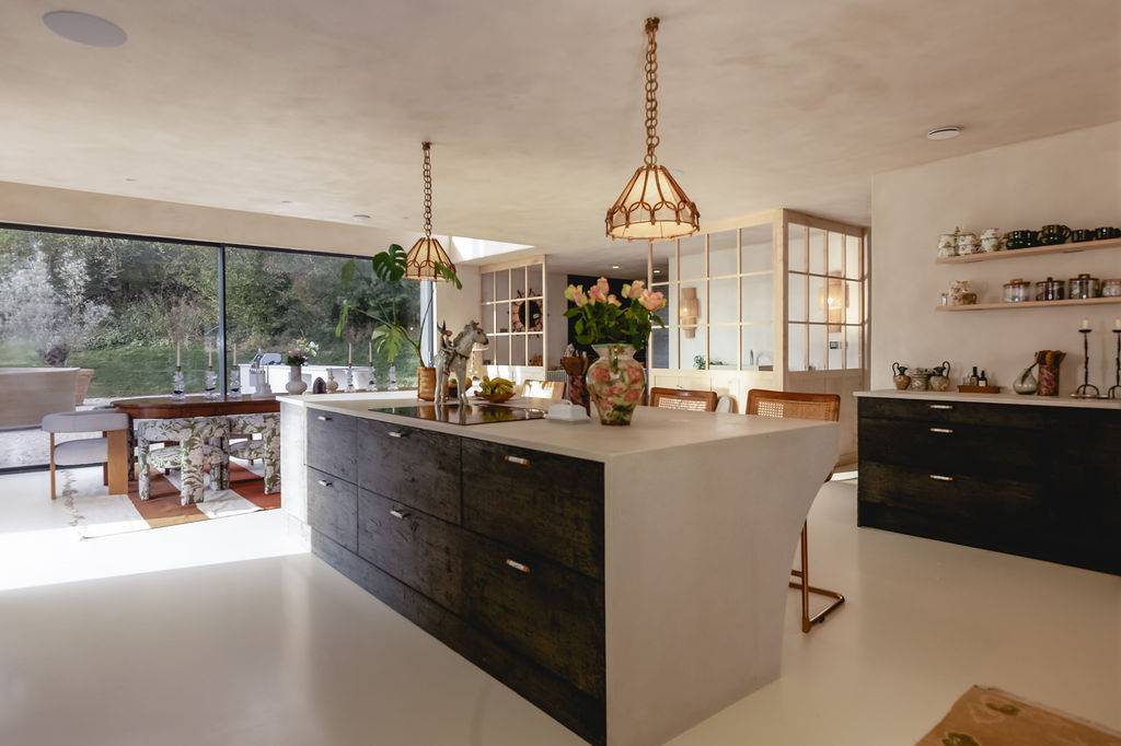 Modern kitchen with a dark wood island unit, marble countertops, brass hardware, and garden window views, Love Locations GU32.