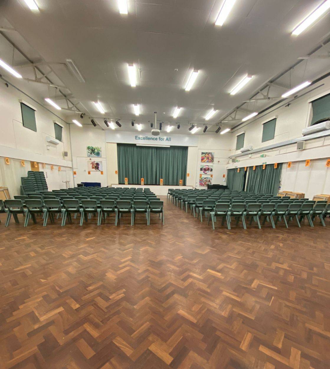 Secondary school assembly hall set up with rows of green chairs facing a performance stage through Love Locations.
