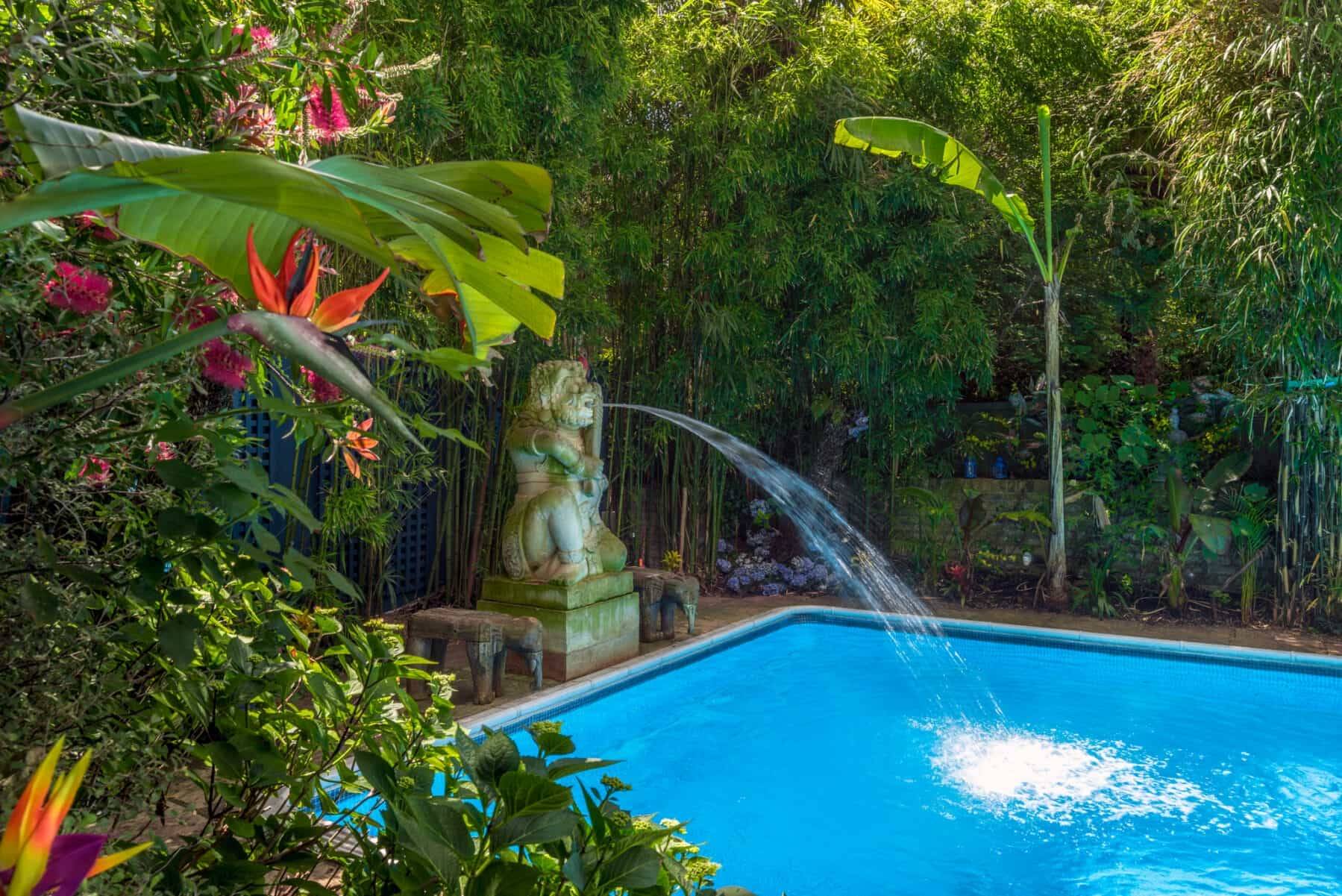 Lush poolside view featuring a stone fountain sculpture cascading water into an outdoor swimming pool, Love Locations SW5.