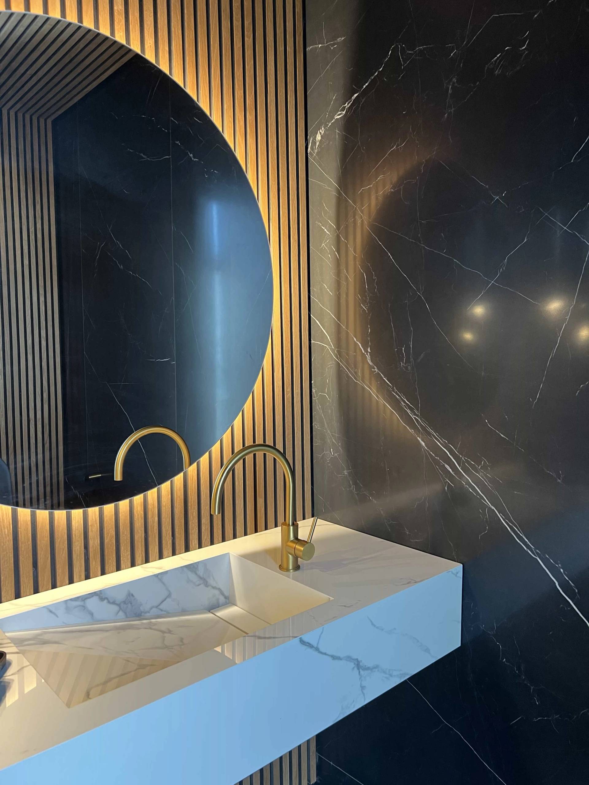 Bespoke cloakroom sink setup with a gold tap, fluted wall panelling, and a circular backlit mirror, Love Locations.