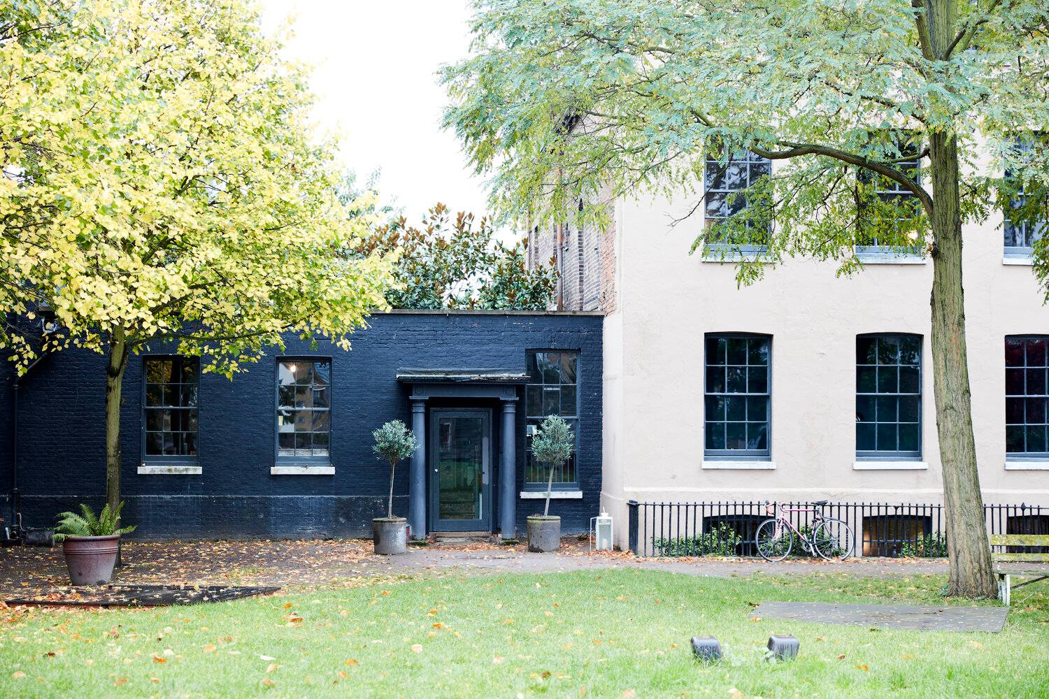 Rear view of a Georgian location home with dark blue painted extensions, manicured lawns, and trees, Love Locations.