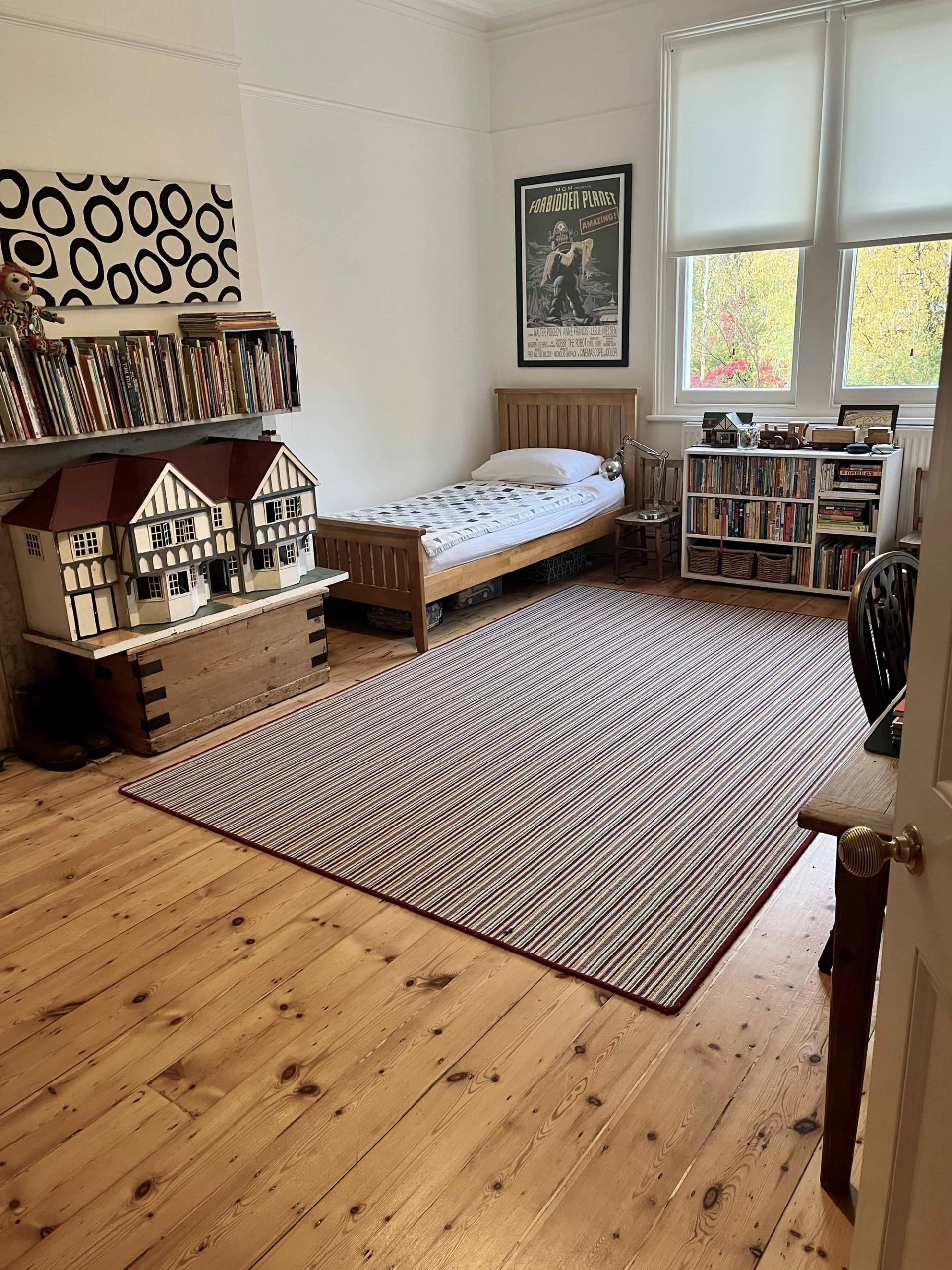 Children's bedroom or nursery with a single wooden bed, vintage dollhouse, striped rug, and exposed brick details, Love Locations SE5.