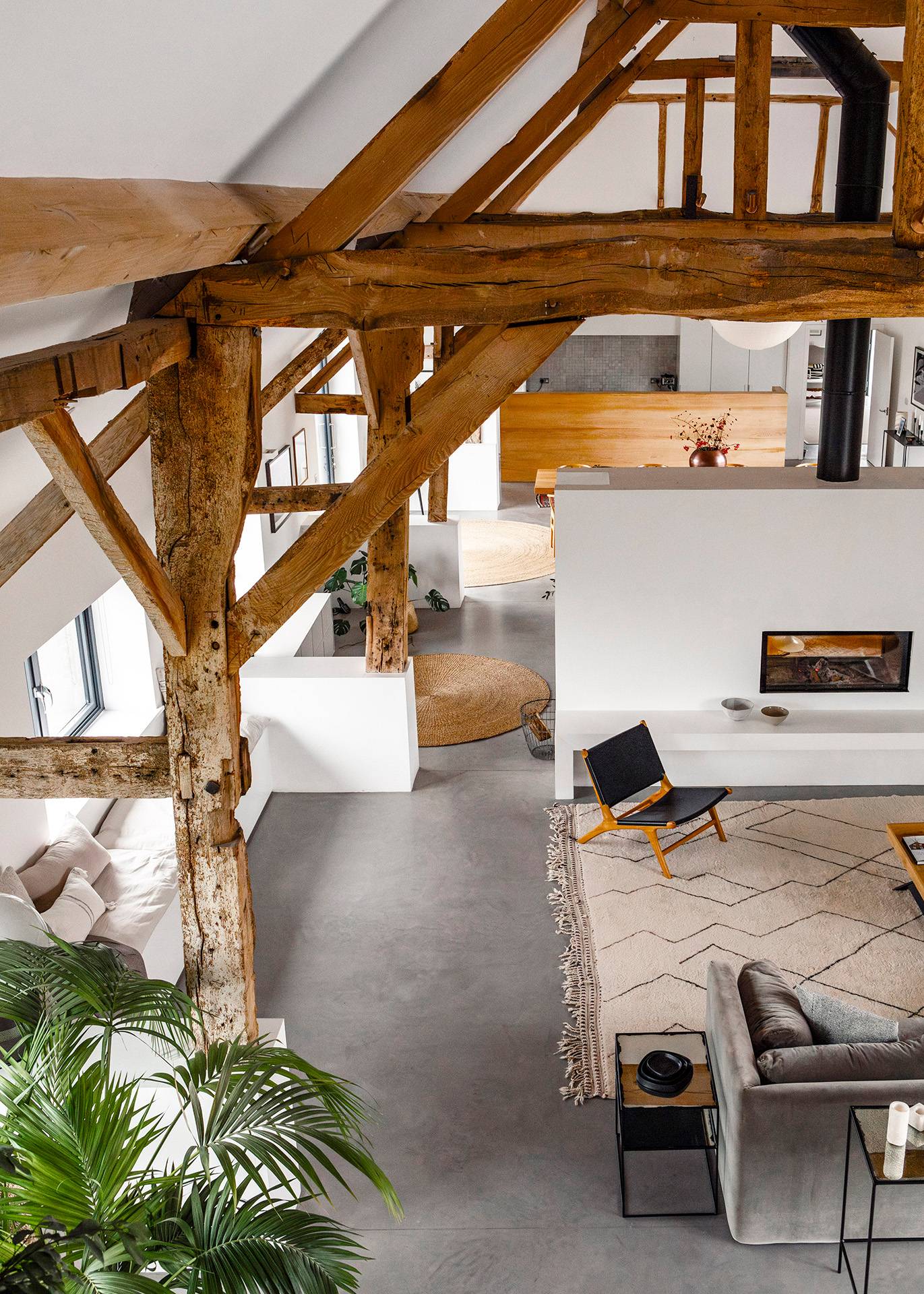 High-angle mezzanine perspective looking down into a vaulted barn living room with exposed timber beams, Love Locations SN8.